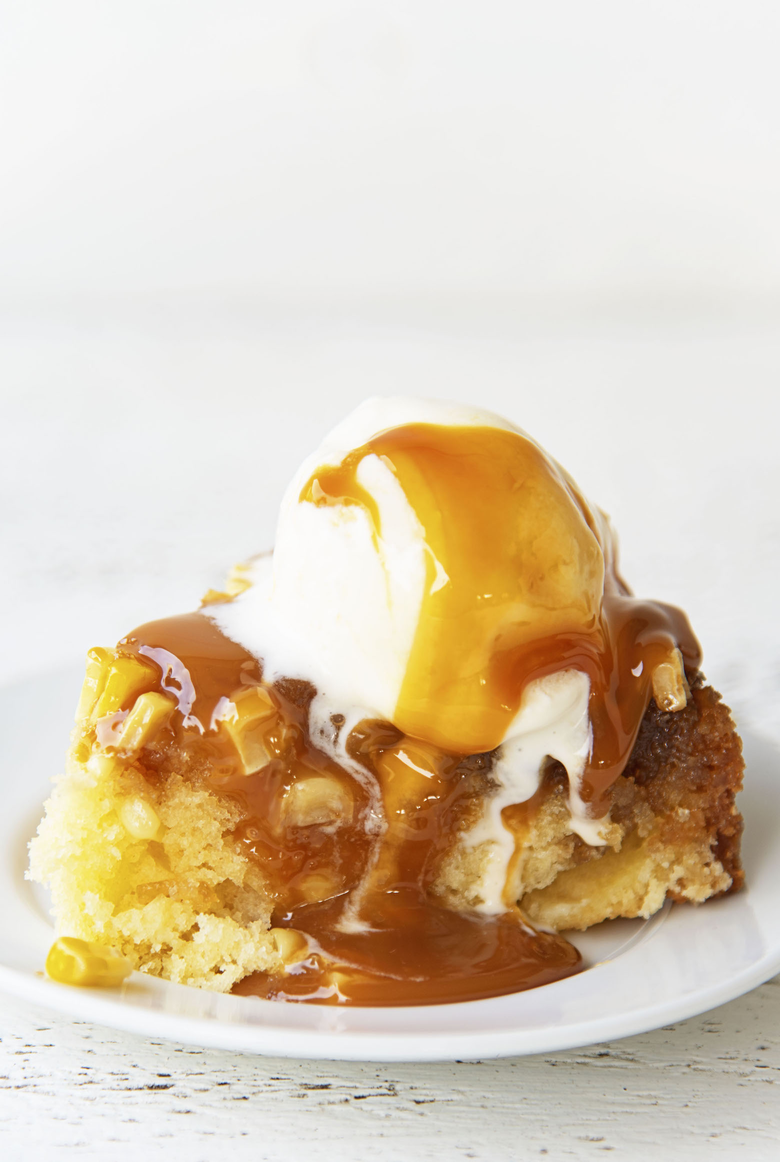 Side view of the upside down cake on a plate with ice cream and caramel sauce dripping down.