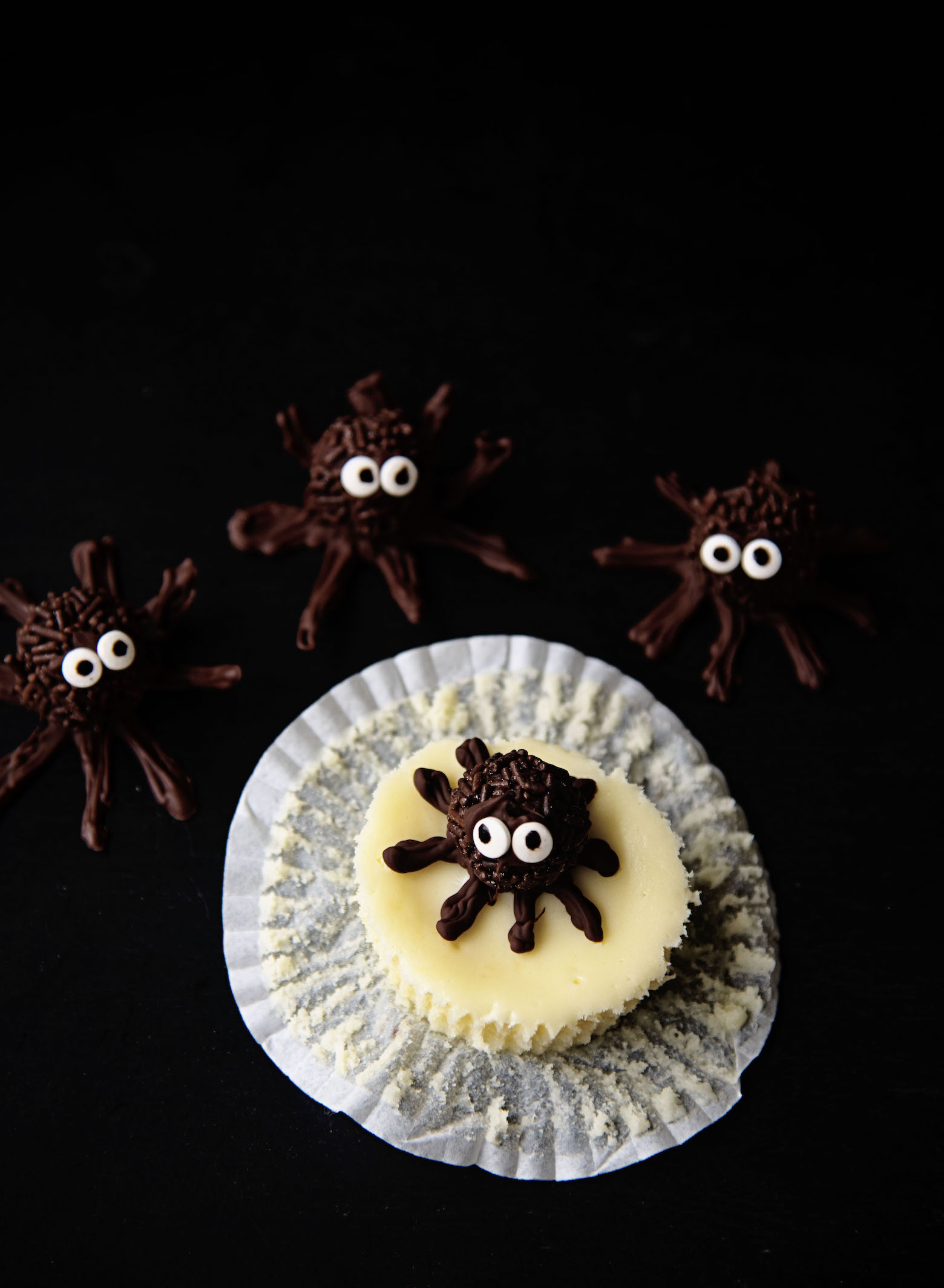 Overhead of a single Chocolate Truffle Spider Cheesecake Bite with the liner pulled away and extra chocolate spiders around it 