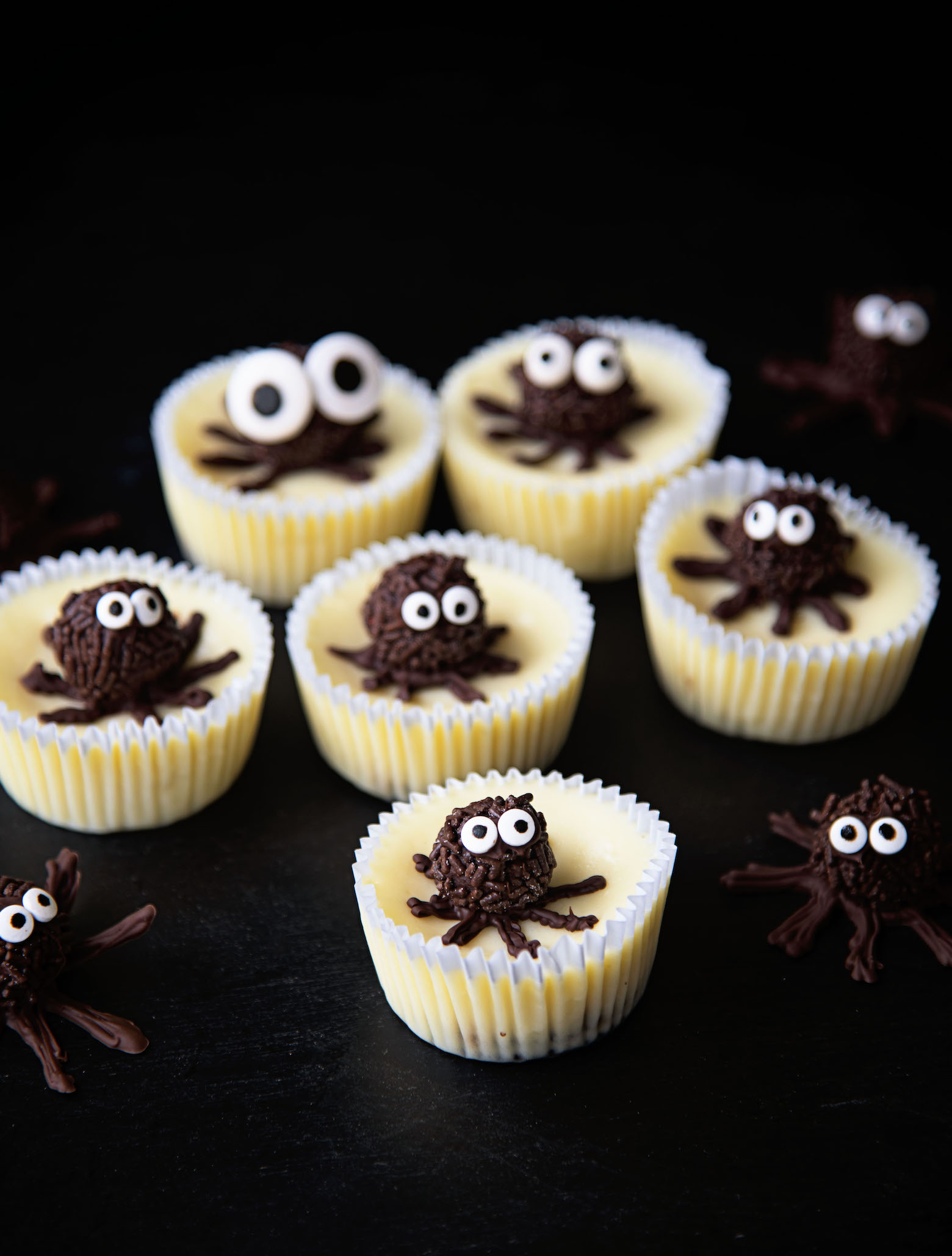 Gathering of six Chocolate Truffle Spider Cheesecake Bites with extra chocolate spiders around