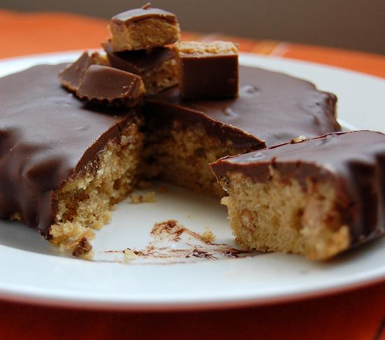 A peanut butter cup cake with slice out of it to expose the center