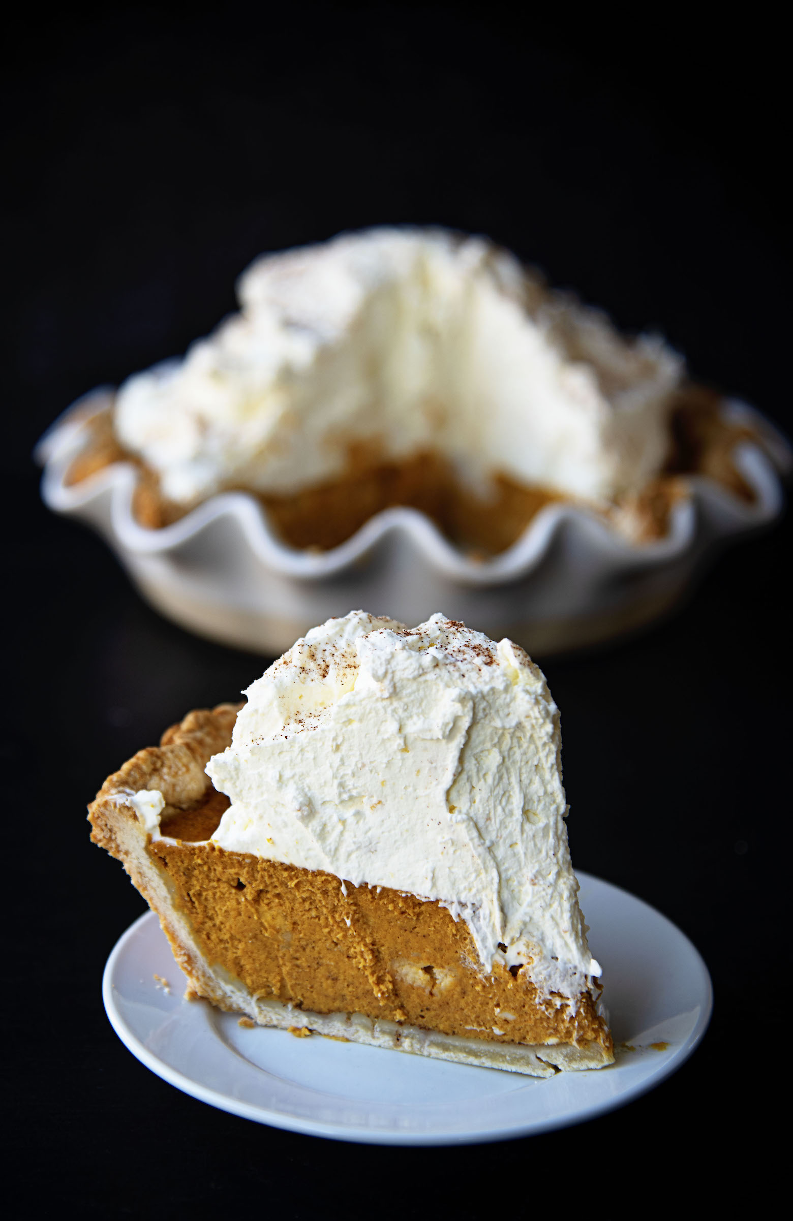 Slice of Snickerdoodle Pumpkin Cream Cheese Pie with the remaining full pie in the background. 