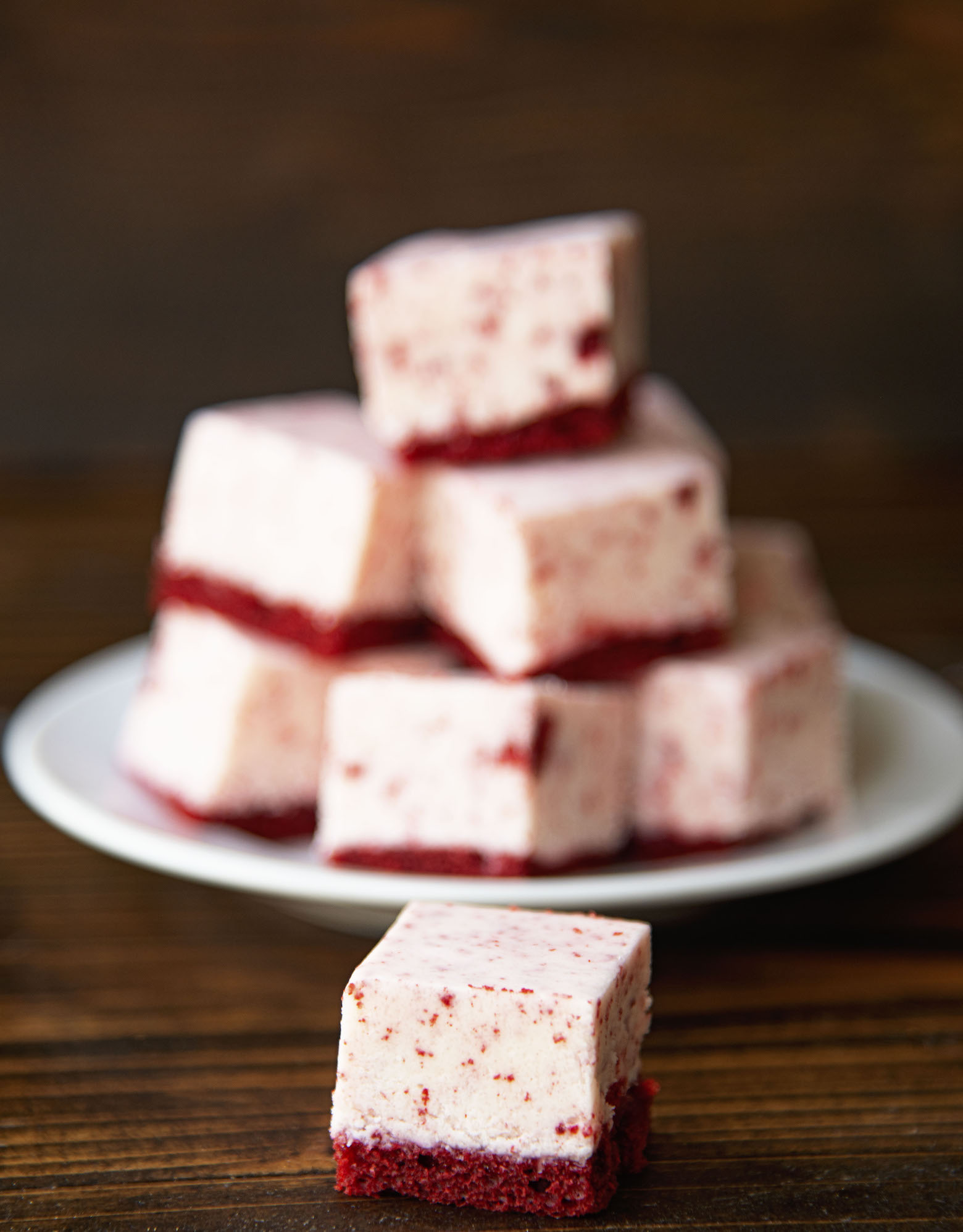 A piece of Cream Cheese Red Velvet Fudge up front with a plate of fudge in the background