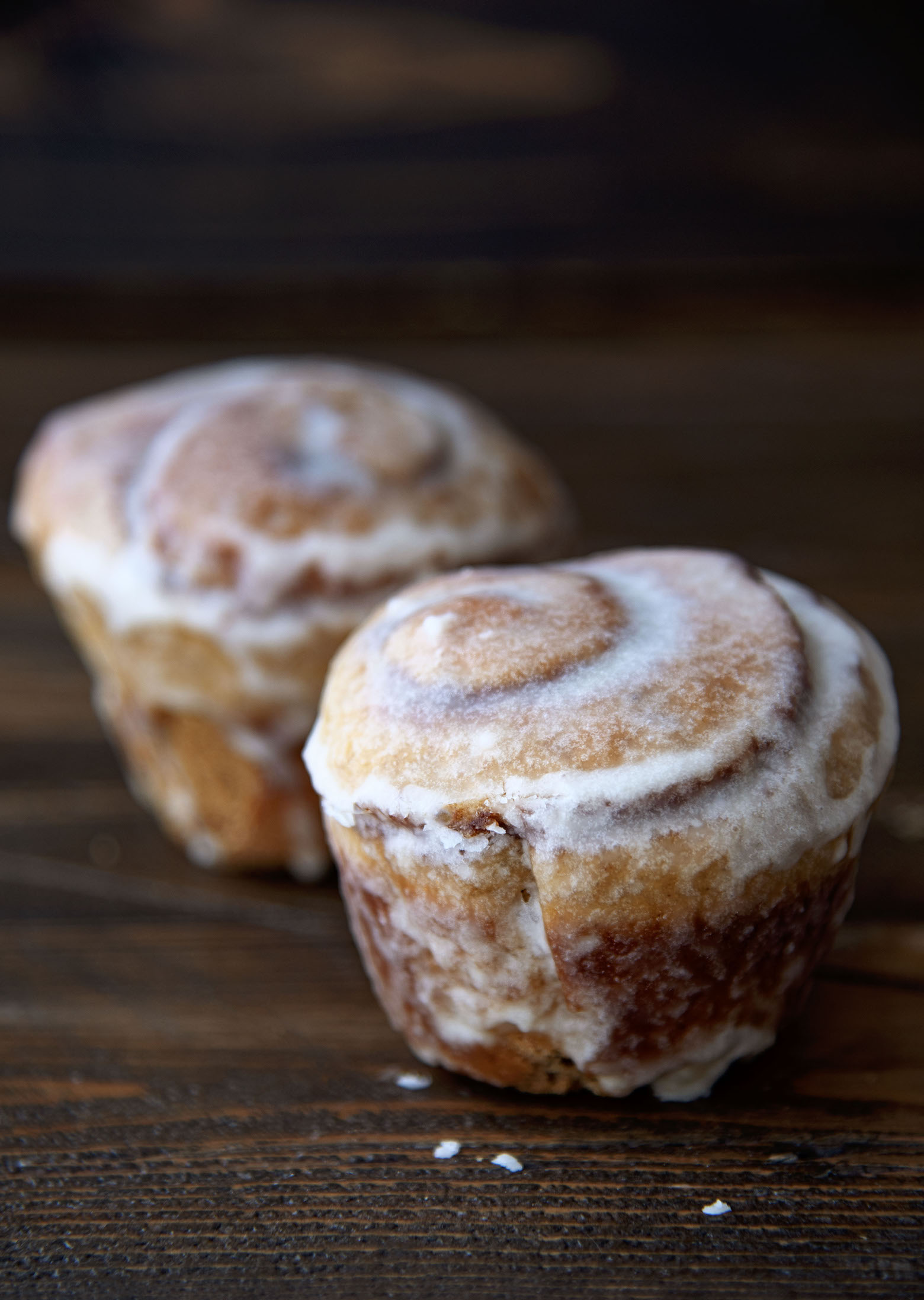 Two Orange Gingerbread Cinnamon Rolls with thinner glaze showing the swirls of the rolls.