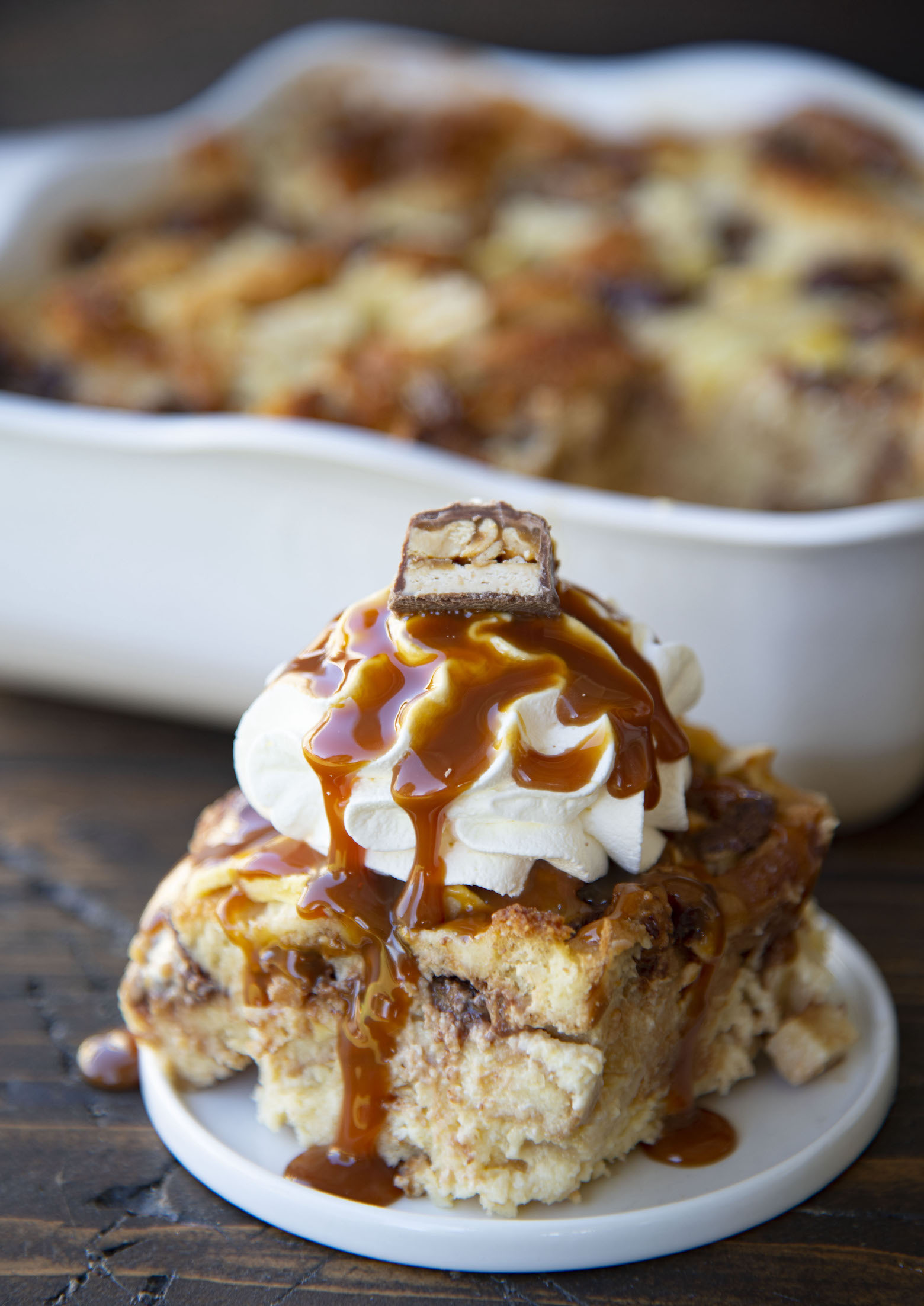 Slice of bread pudding on a plate with remaining bread pudding behind it. 