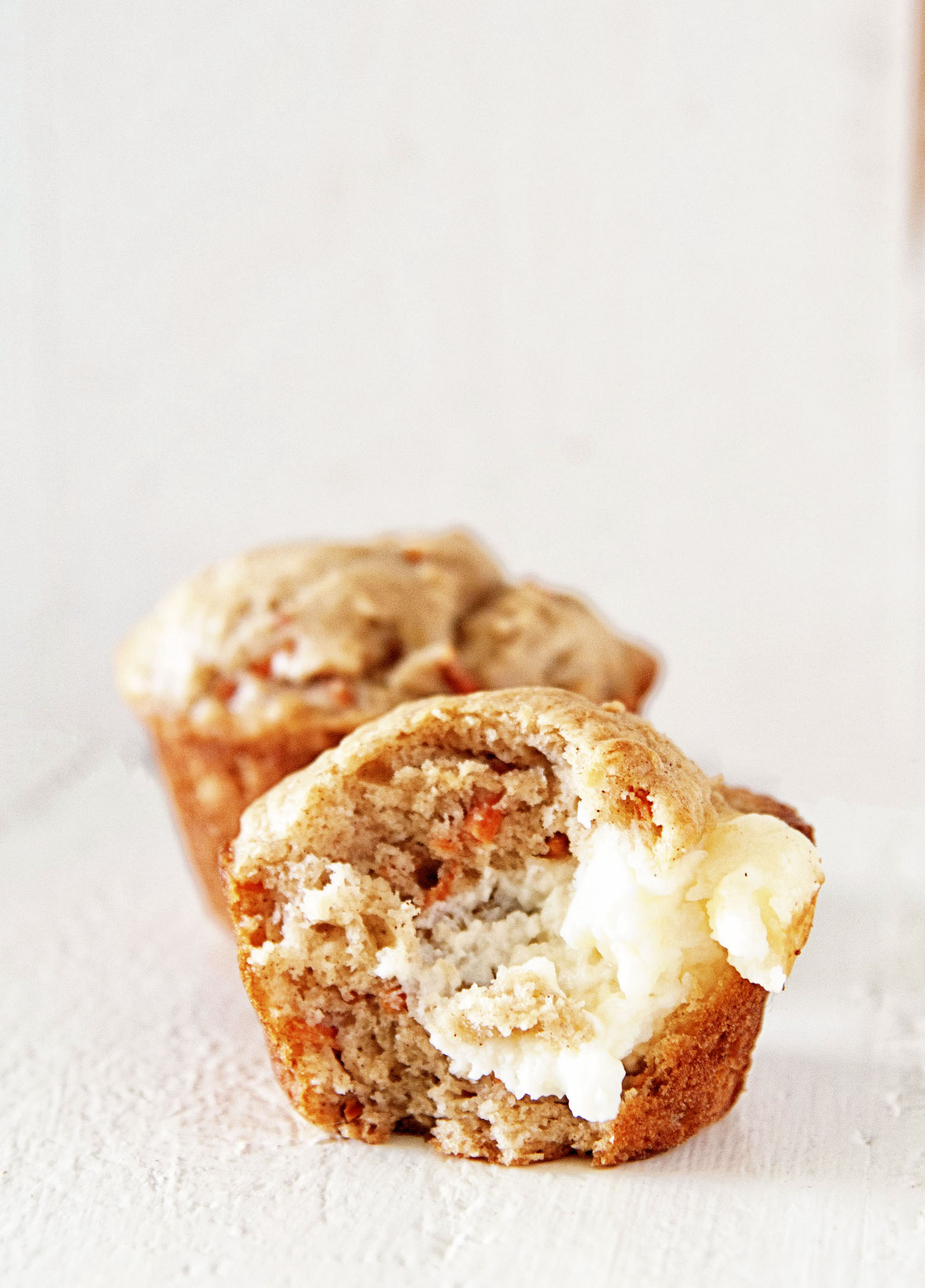 Two Carrot Cake Cream Cheese Muffins with the focus on the first muffin that has a bite out of it. 