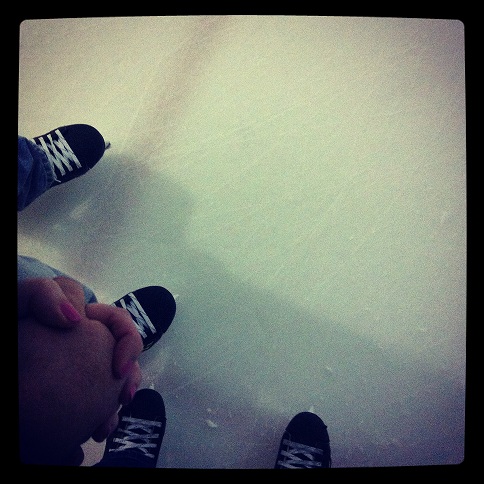 Looking down at two sets of hockey skates on ice with couple holding hands
