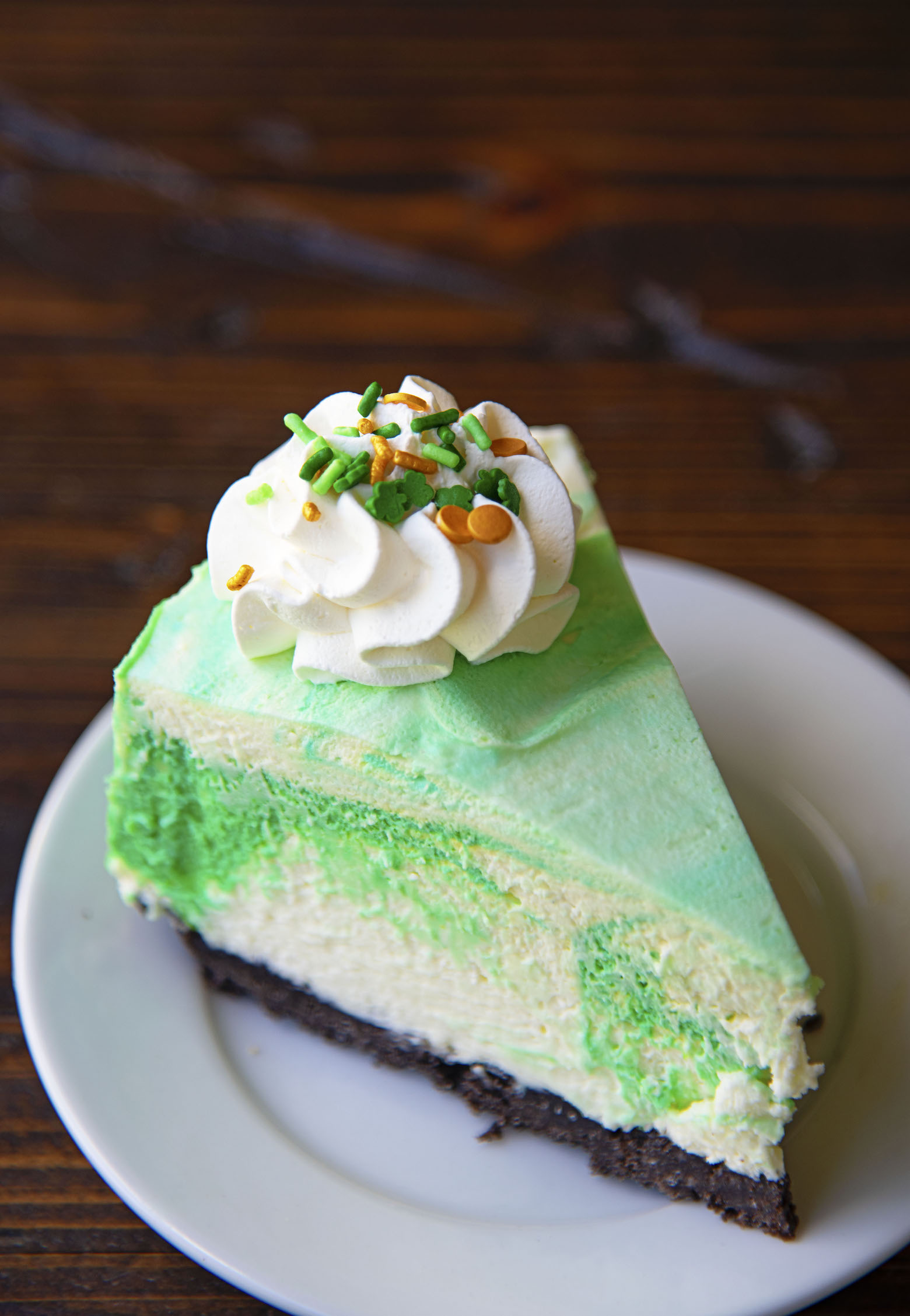 Slice of Vanilla Mint Mousse Cake on a small white plate with a brown background.