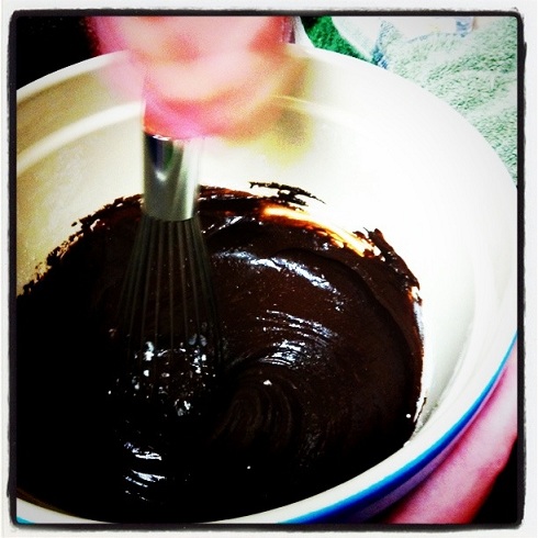 Bowl with brownie batter in it with a hand holding a whisk.