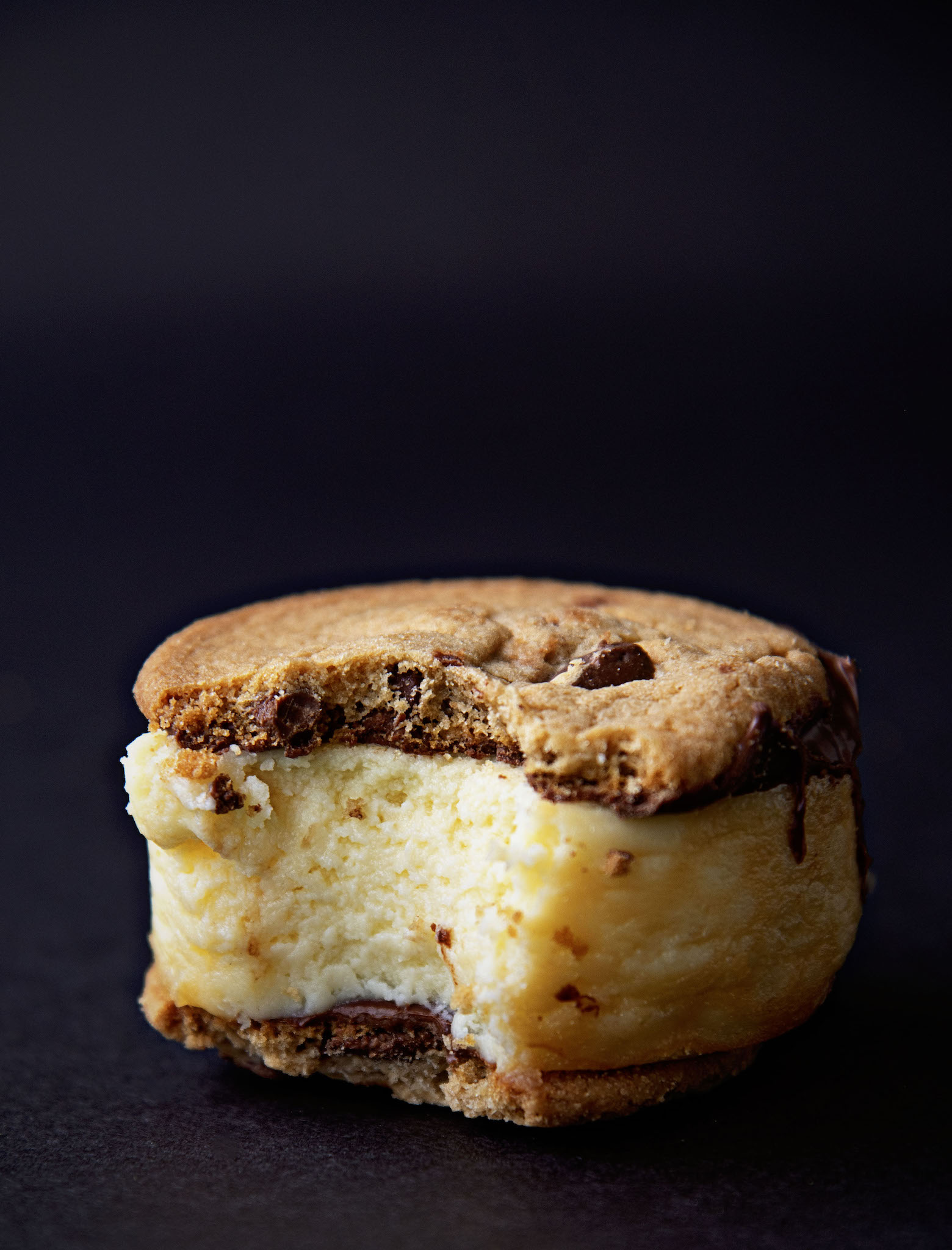 Single Chocolate Chip Cookie Cheesecake Sandwich with bite taken out of it. Black background. 