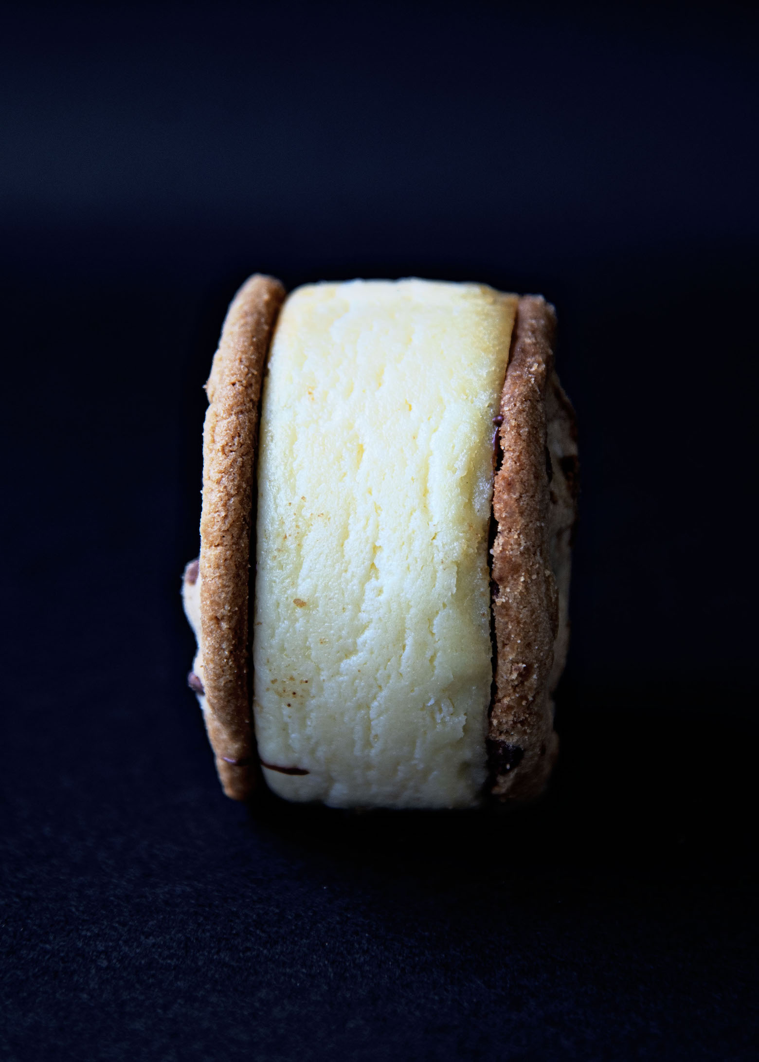 Single Chocolate Chip Cookie Cheesecake Sandwich turned on it's side. Black background.