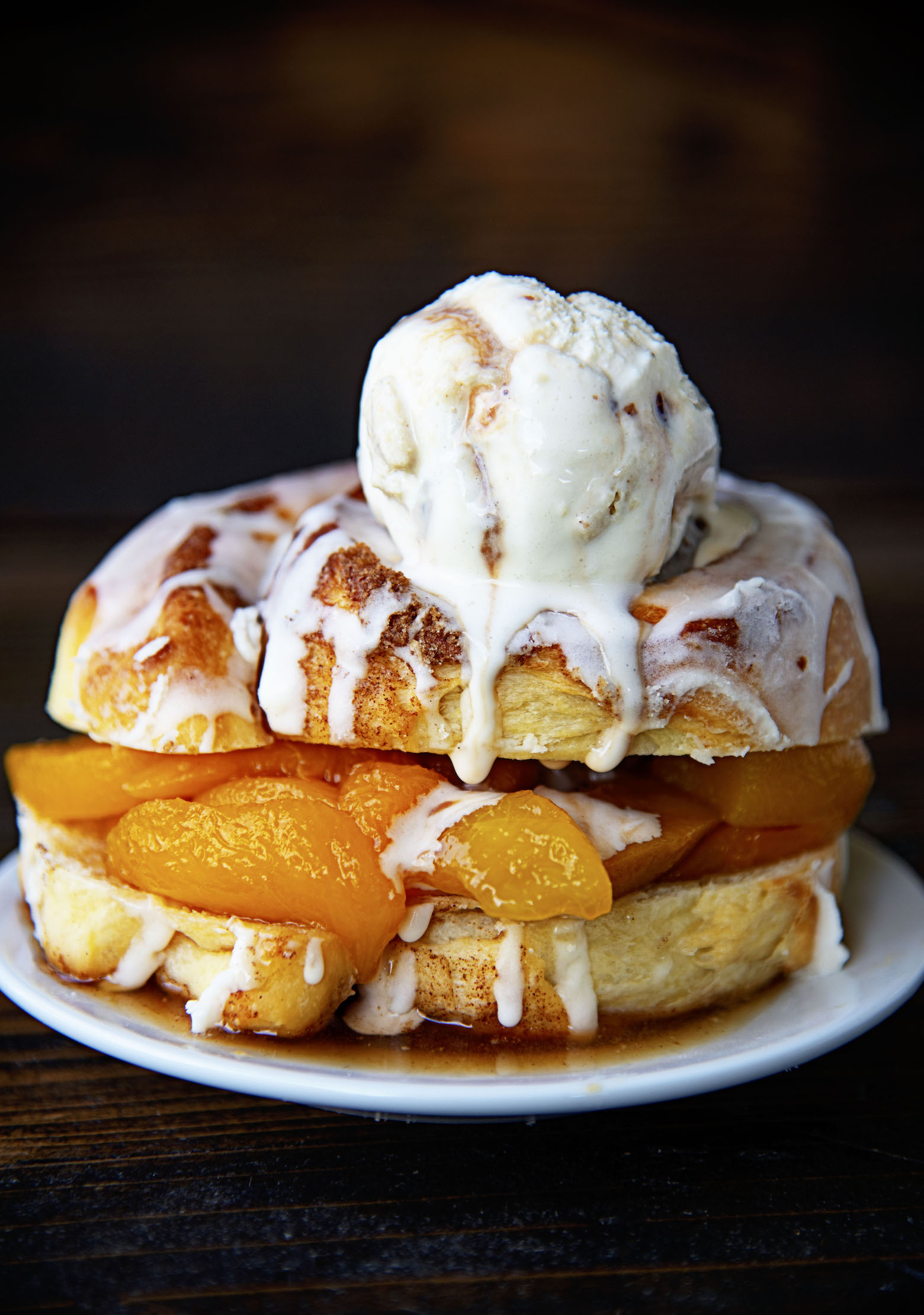 Side view of Cinnamon Roll Peach Shortcake with ice cream on top dripping down with peach pieces poking out. 