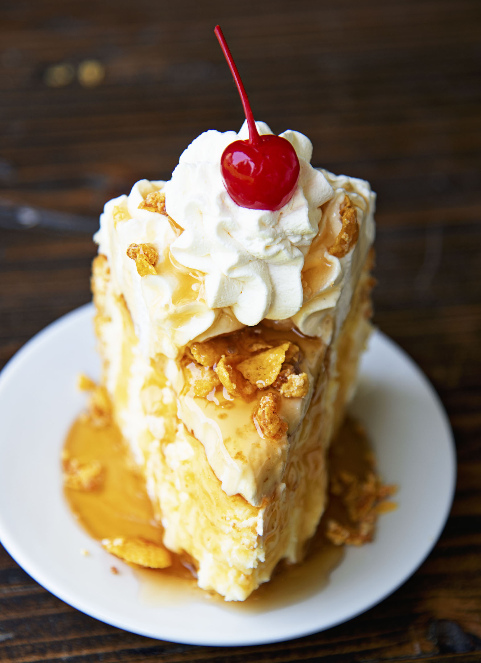 Close up of single piece of cheesecake with the focus on the whipped cream and cherrry.