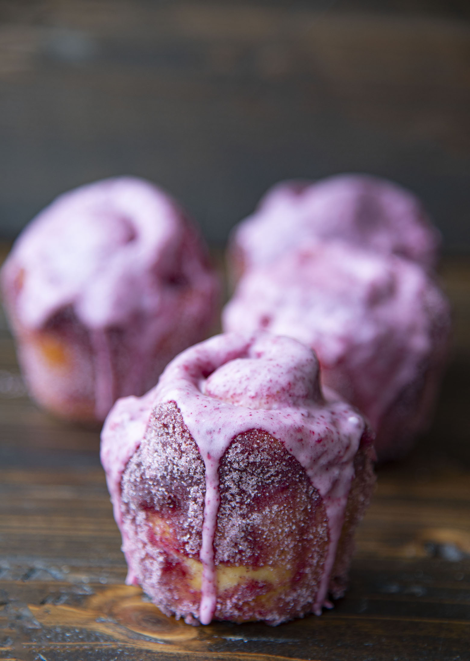 Side view of a bun with purple glaze dripping down with three buns in the background behind it.