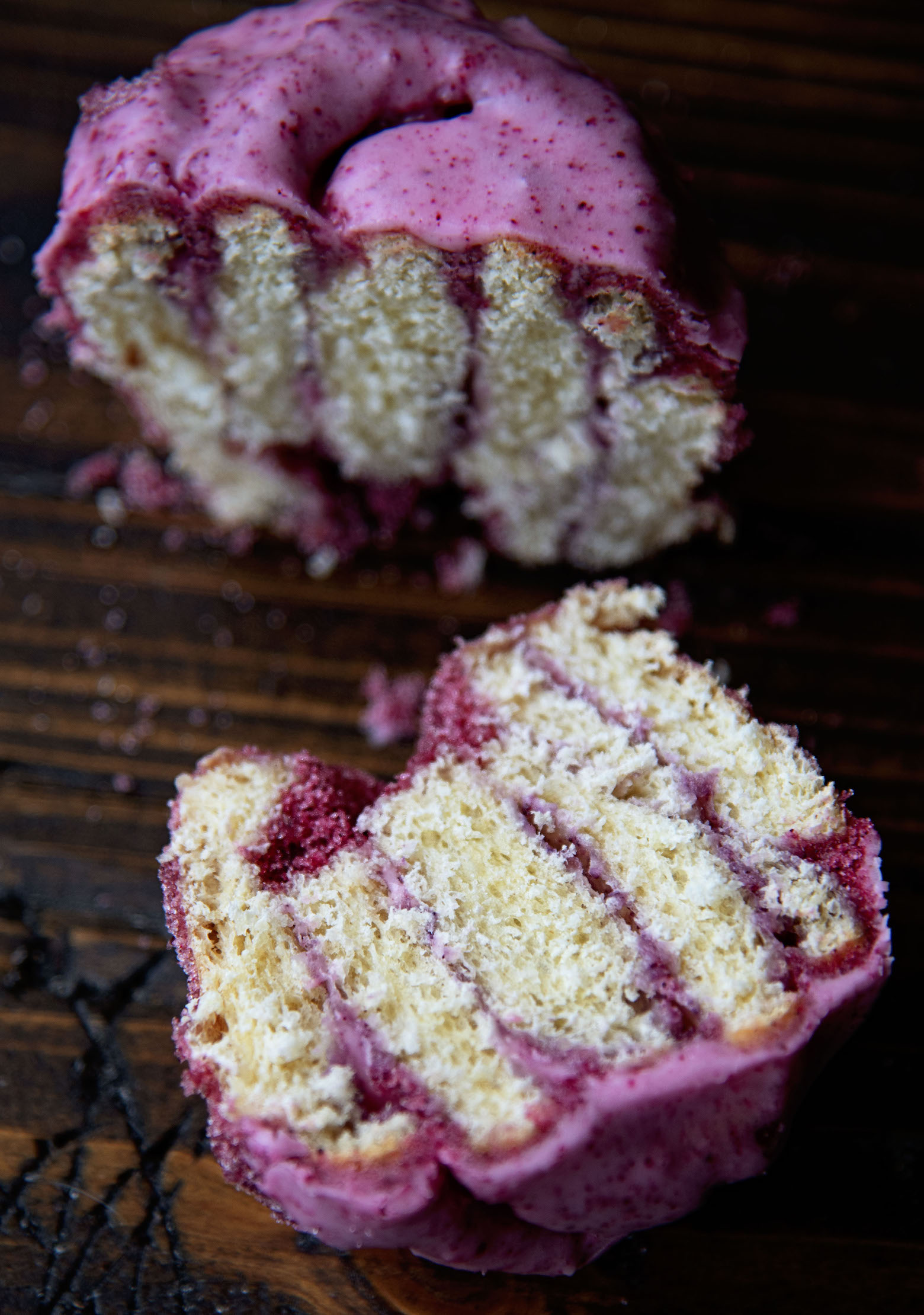 A sliced open Kir Royale Sugar Bun with half the bun standing up and the other laying on the wood surface exposing the filling of the bun.