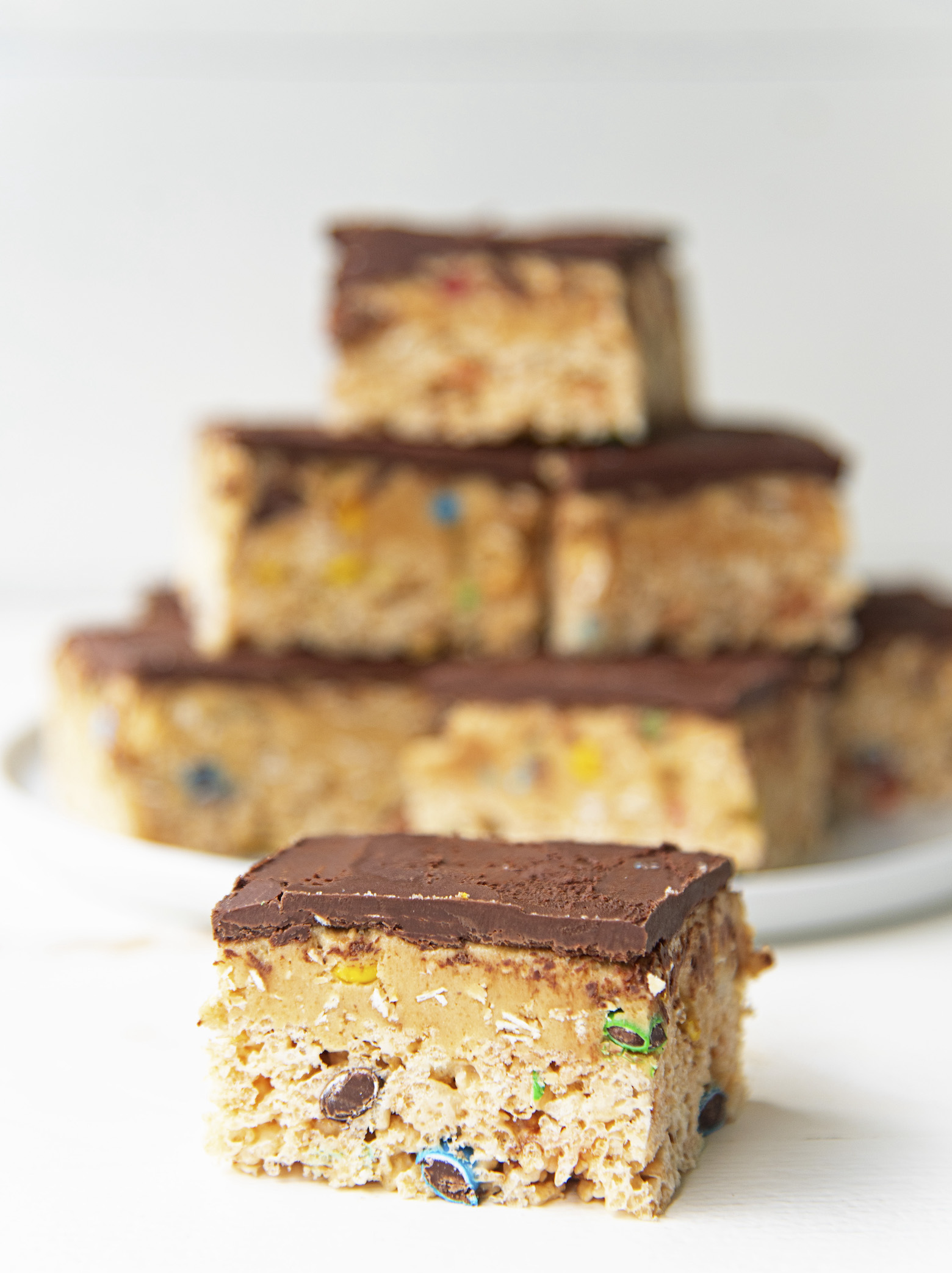 A single Monster Cookie Dough Rice Krispie Treat in front of a plate stacked with more treats. 