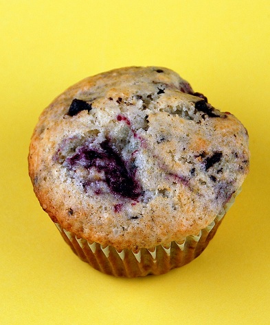 Single whole Raspberry Chocolate Almond Muffin against a yellow background.