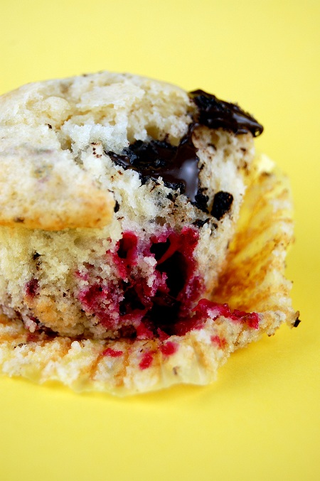 Side view of Raspberry Chocolate Almond Muffin with the muffin liner pulled away exposing the berries and chocolate in the muffin. Yellow background. 