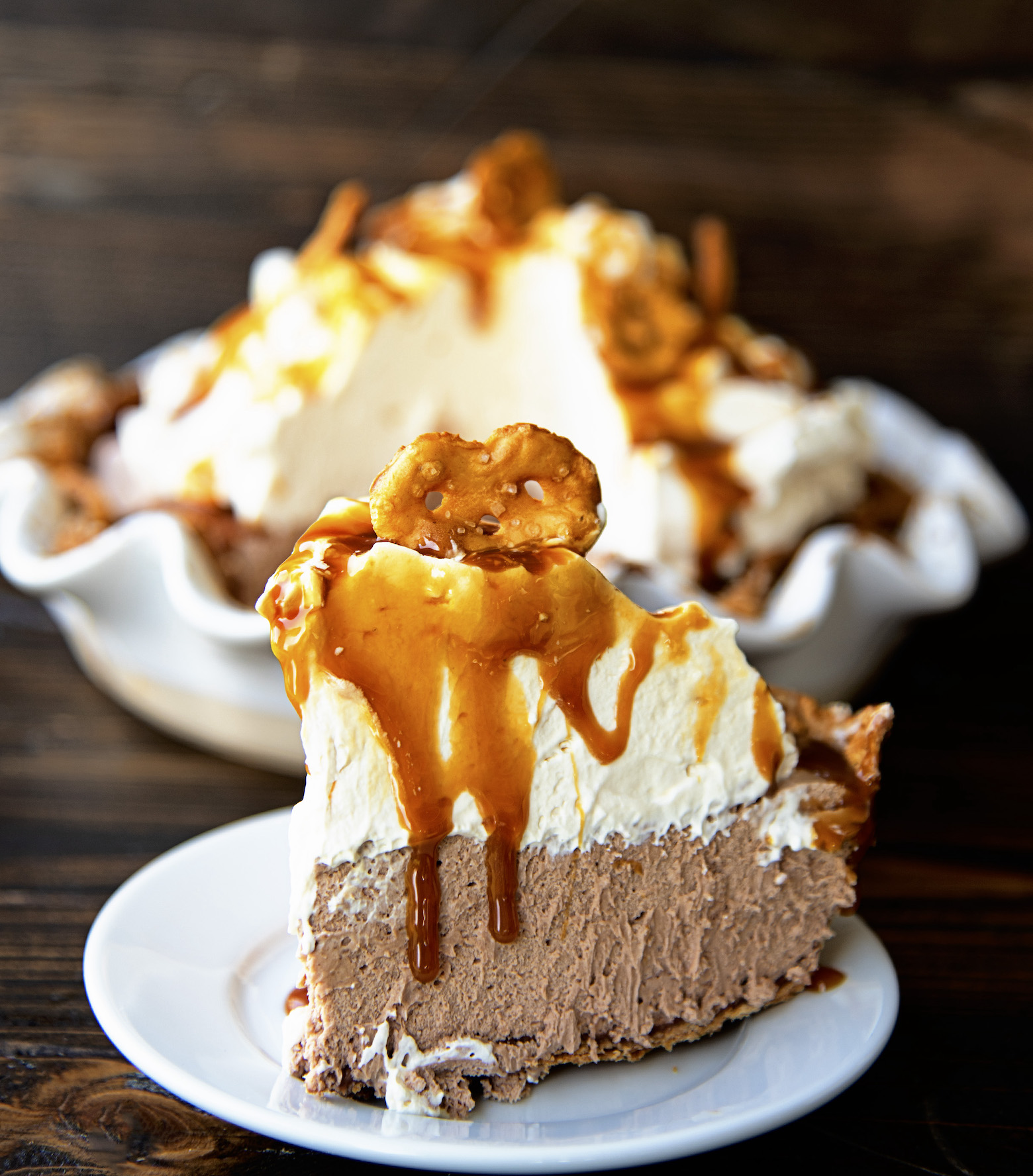 Close up of the Chocolate Caramel Pretzel Pie on a small plate with caramel dripping down with remaining pie in the background. 