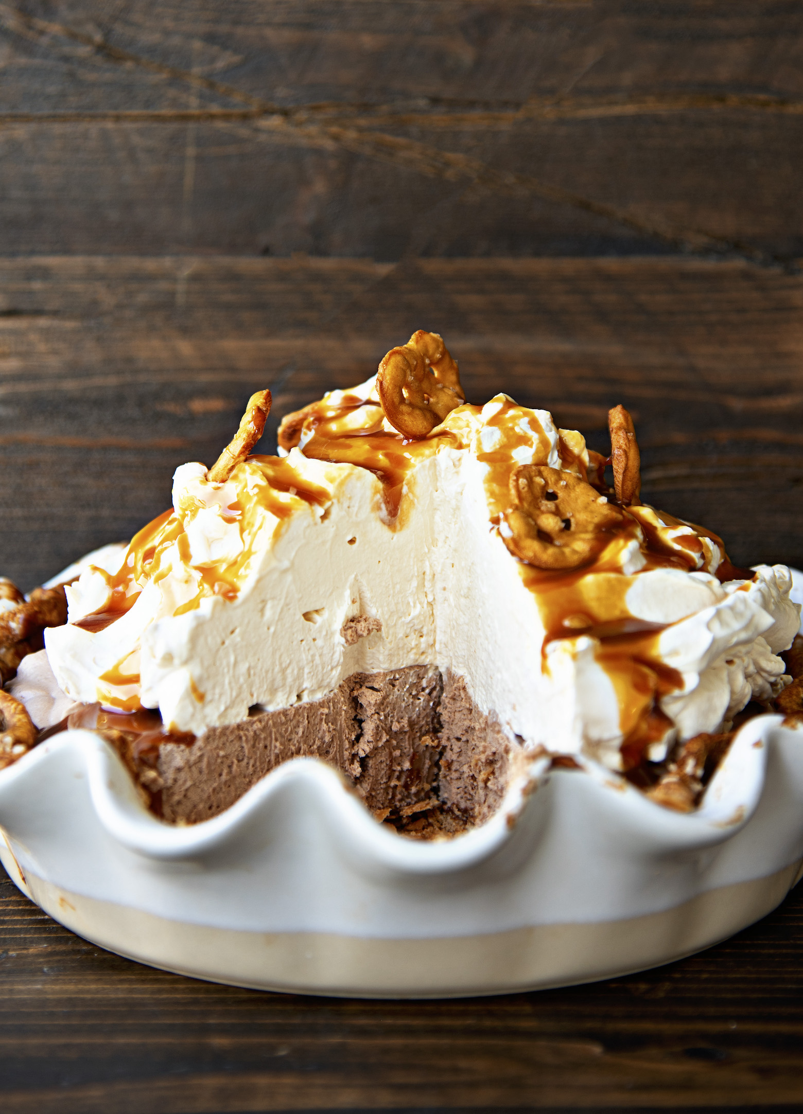Side view of the pie with a piece taken out. Focus on the piled up whipped cream on top of the chocolate caramel filling.