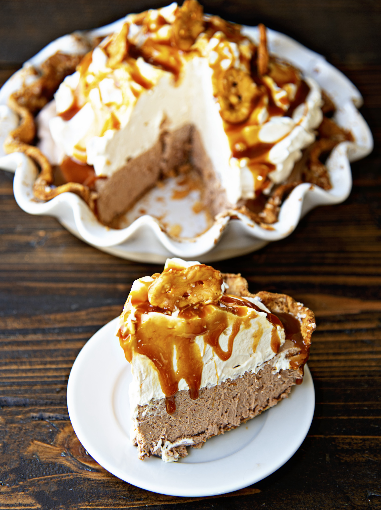 Chocolate Caramel Pretzel Pie on a small plate with caramel dripping down with remaining pie in the background. 