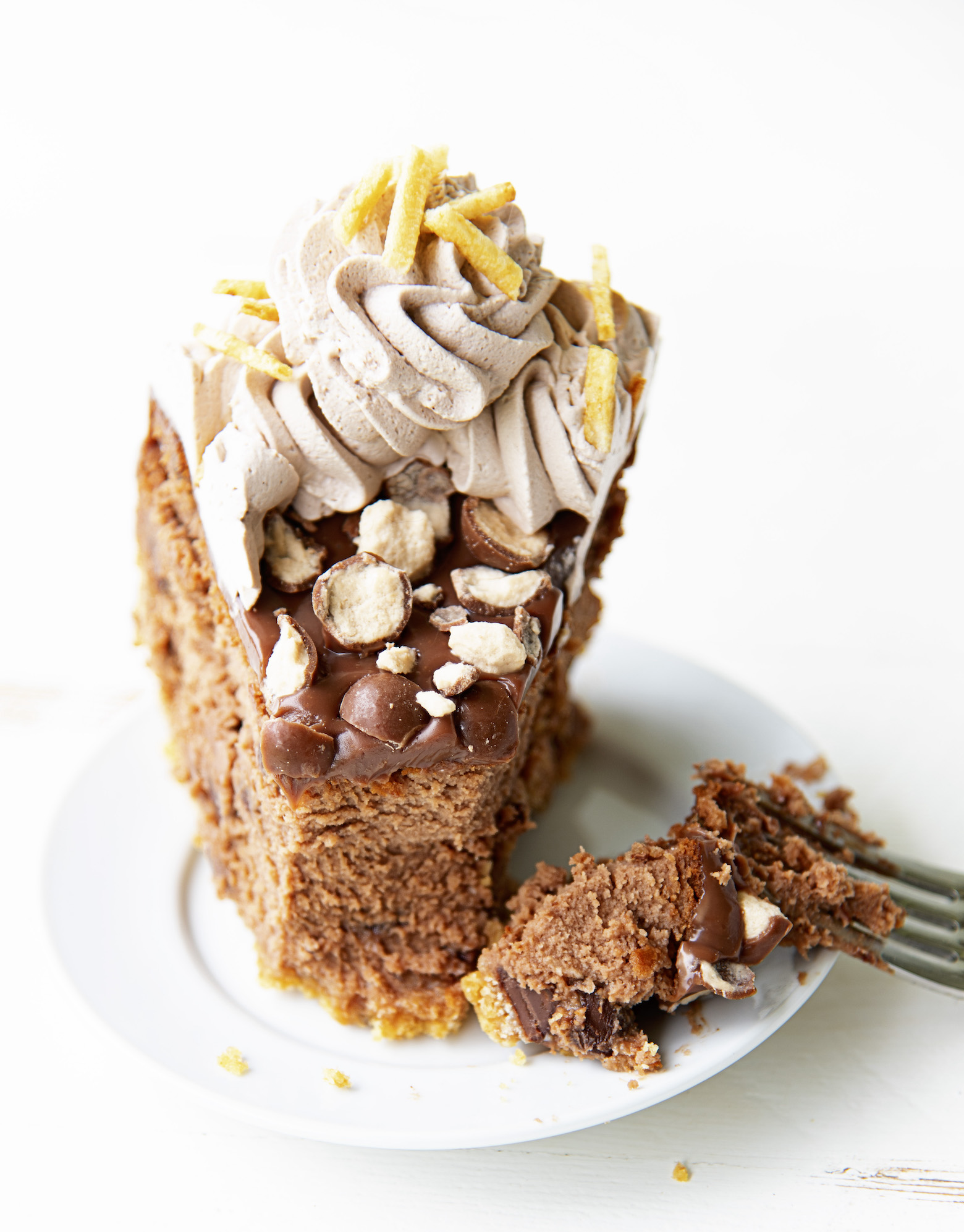 Shot of a single slice of cheesecake with a fork having cut into the cheesecake, with cheesecake still on the fork. Focus is on the fork with the cheesecake.