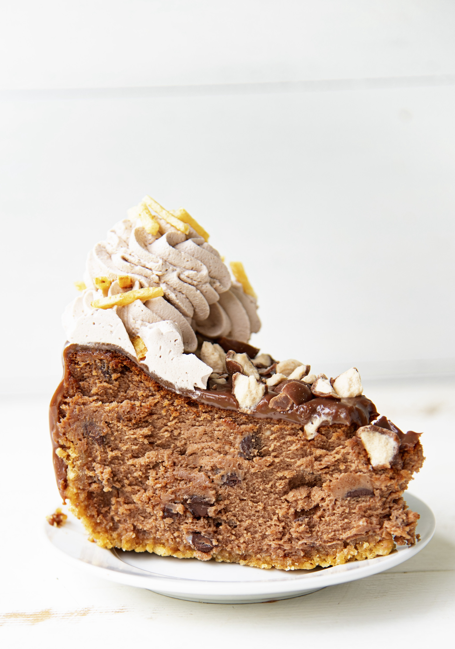 Side shot of a single piece of Chocolate Malt French Fry Cheesecake on a small white plate. 