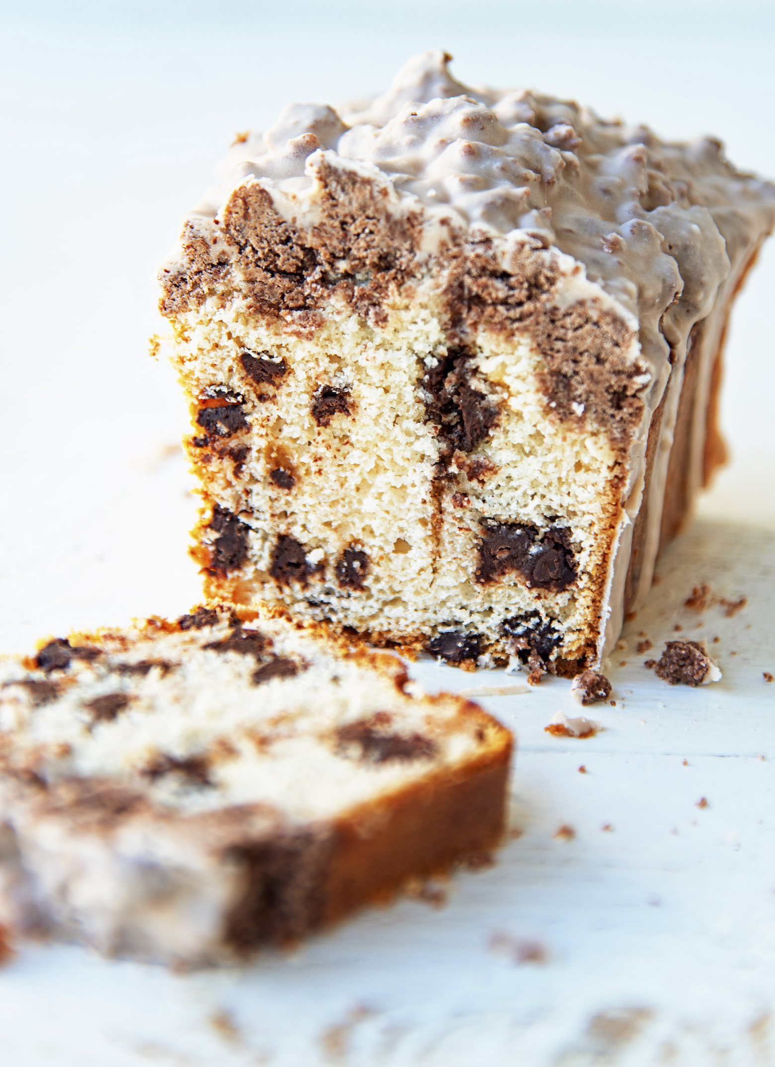 Side view of a single crumb cake with a slice out in front of it exposing the chocolate chip filling. 