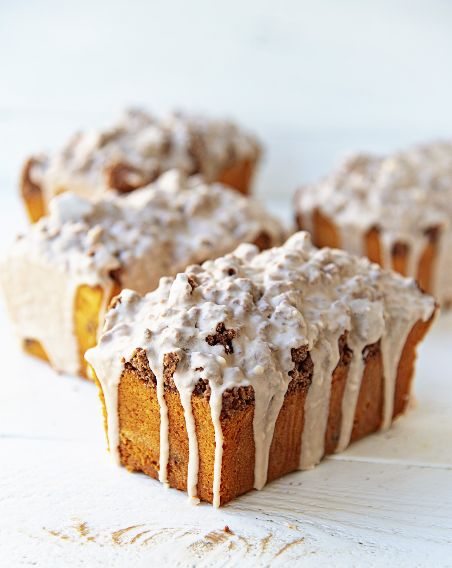 Four Chocolate Milkshake Crumb Cakes, whole, with glaze dripping down on them. Focus on the first crumb cake. 