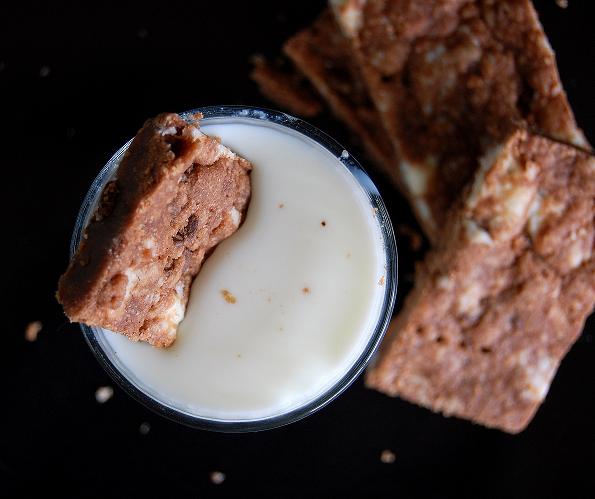 Overhead shot of three pieces of shortbread around a glass of milk. The glass of milk has a piece of shortbread in it. 