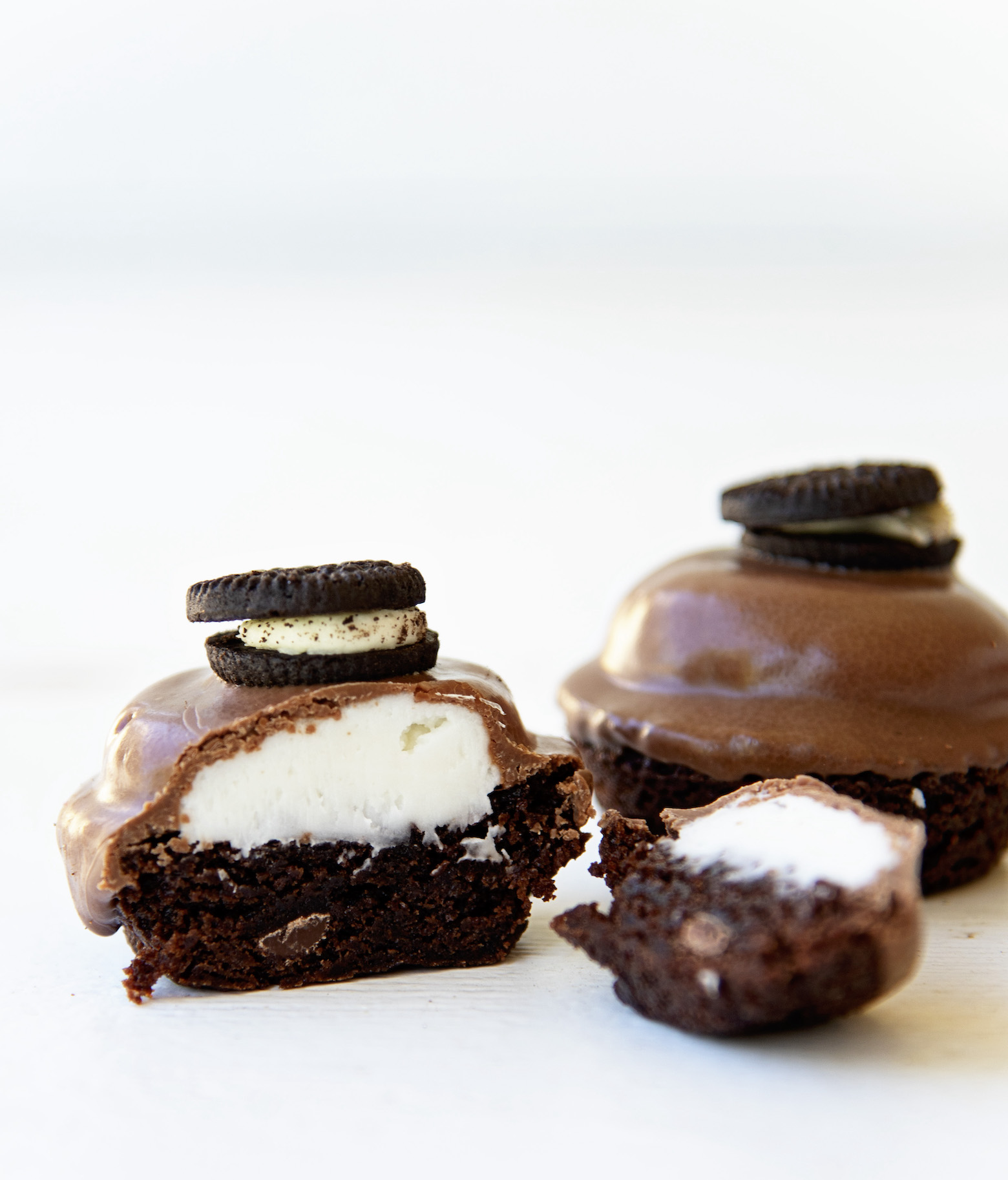 Two Double Stuffed Brownie Bites. One whole and off to the side. With the main bite being but in half. one half is upright exposing the filling. The other is lying next to it. 