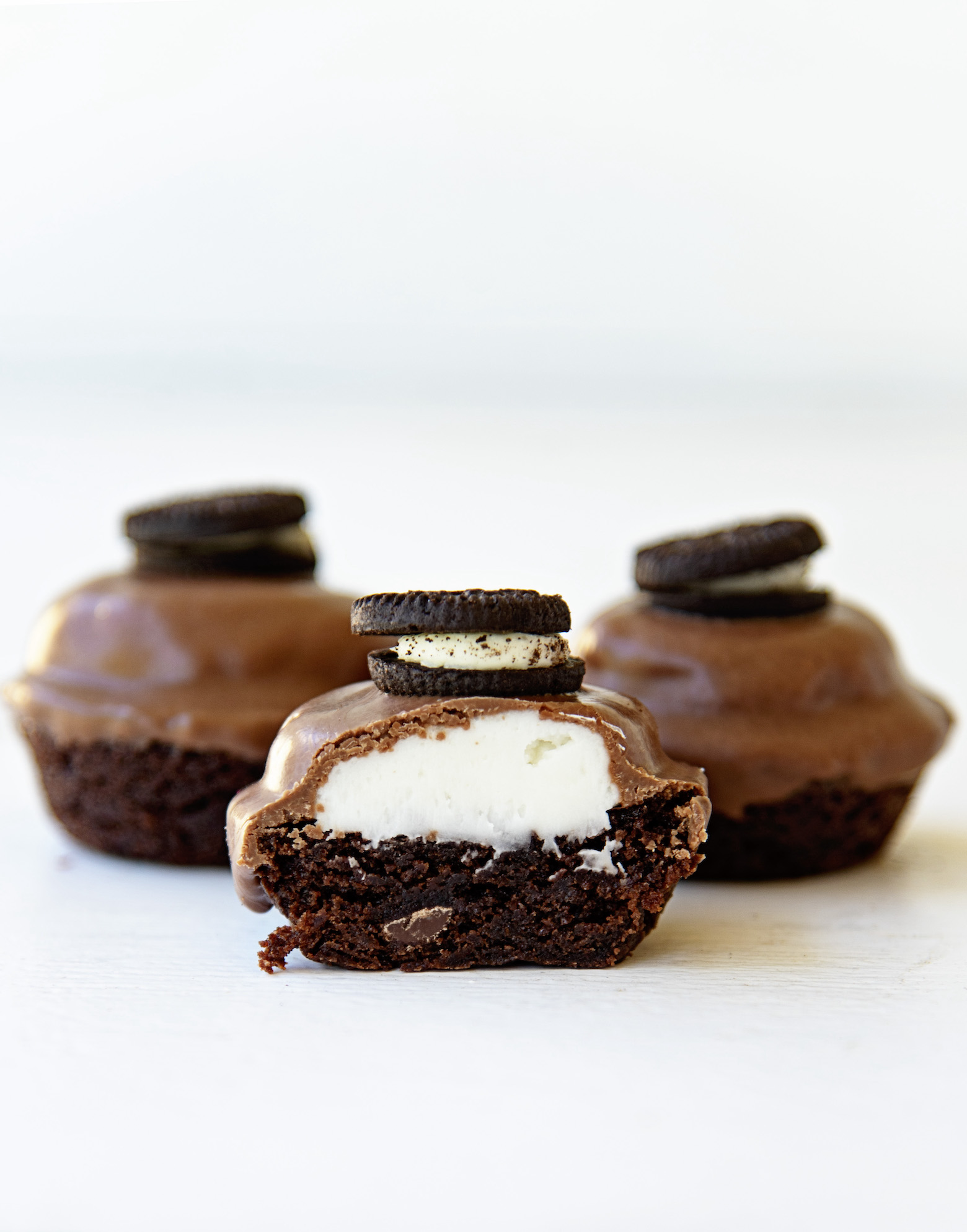 Three brownie bites with two in the back and one front and center. The one in the center is cut in half with the cream filling exposed. 