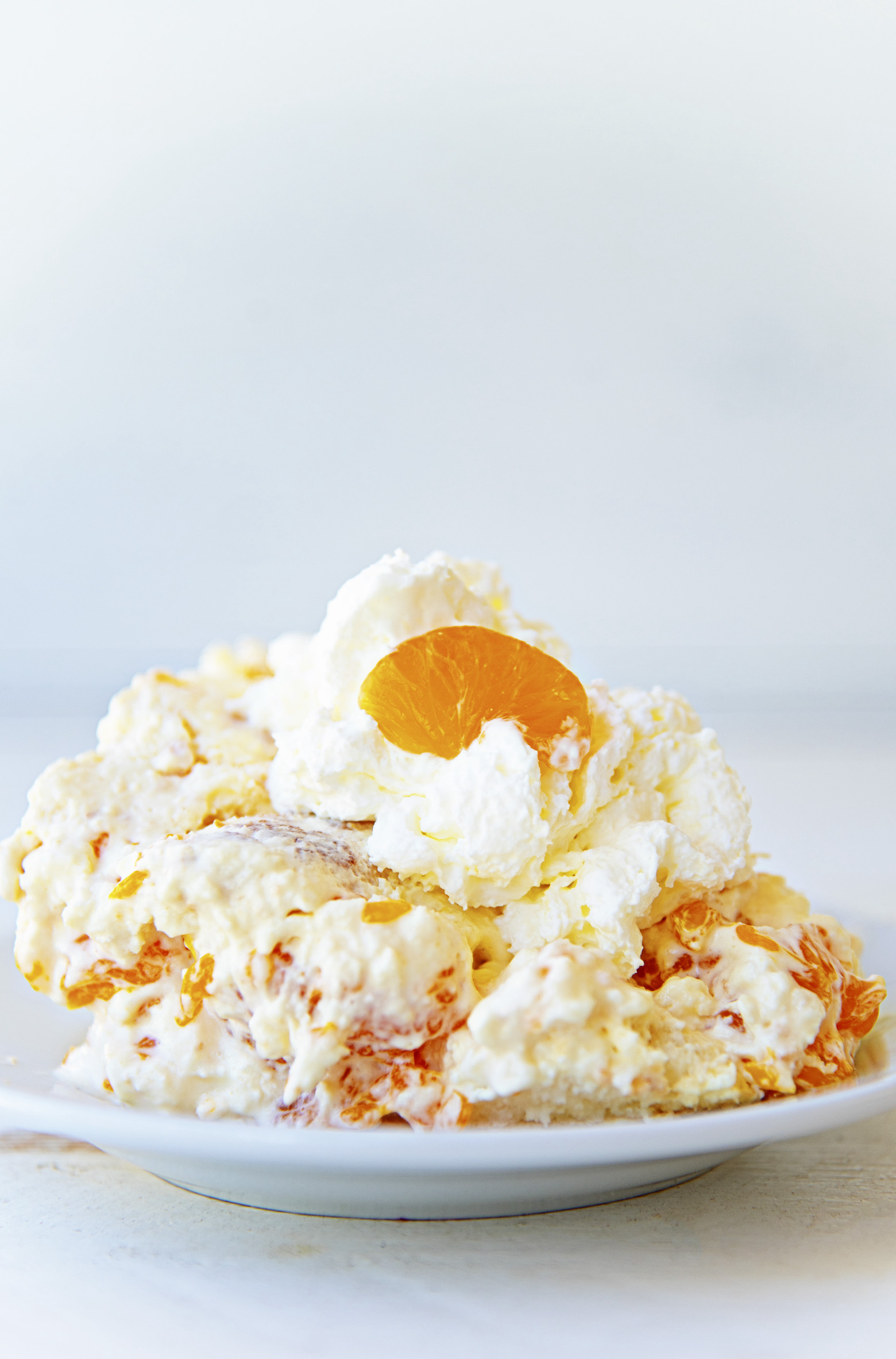 Close up of angel dessert on a small white plate with whipped cream and a small orange slice on top. 