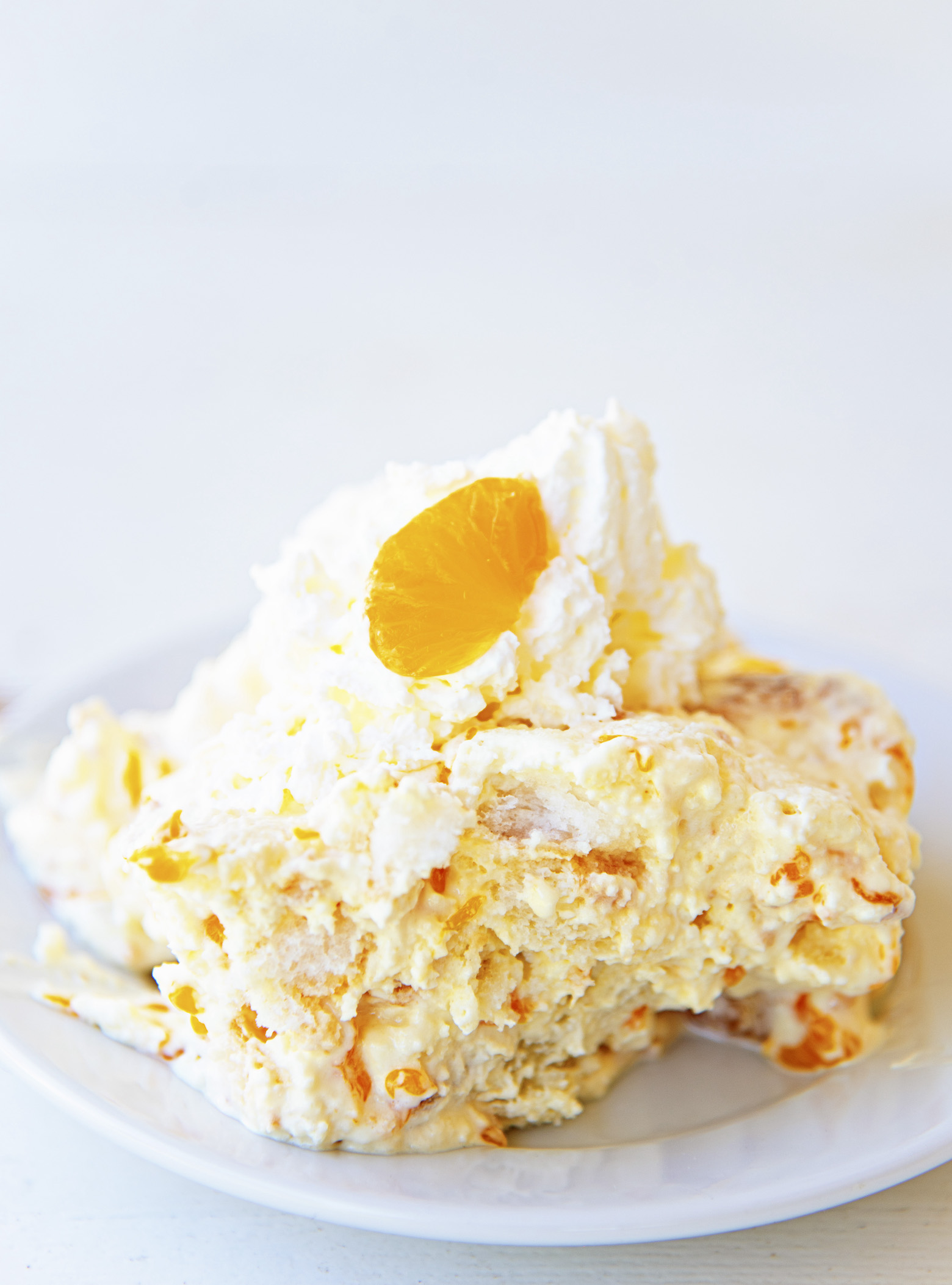 Scoop of angel dessert on a small white plate with whipped cream and a small orange slice on top. 