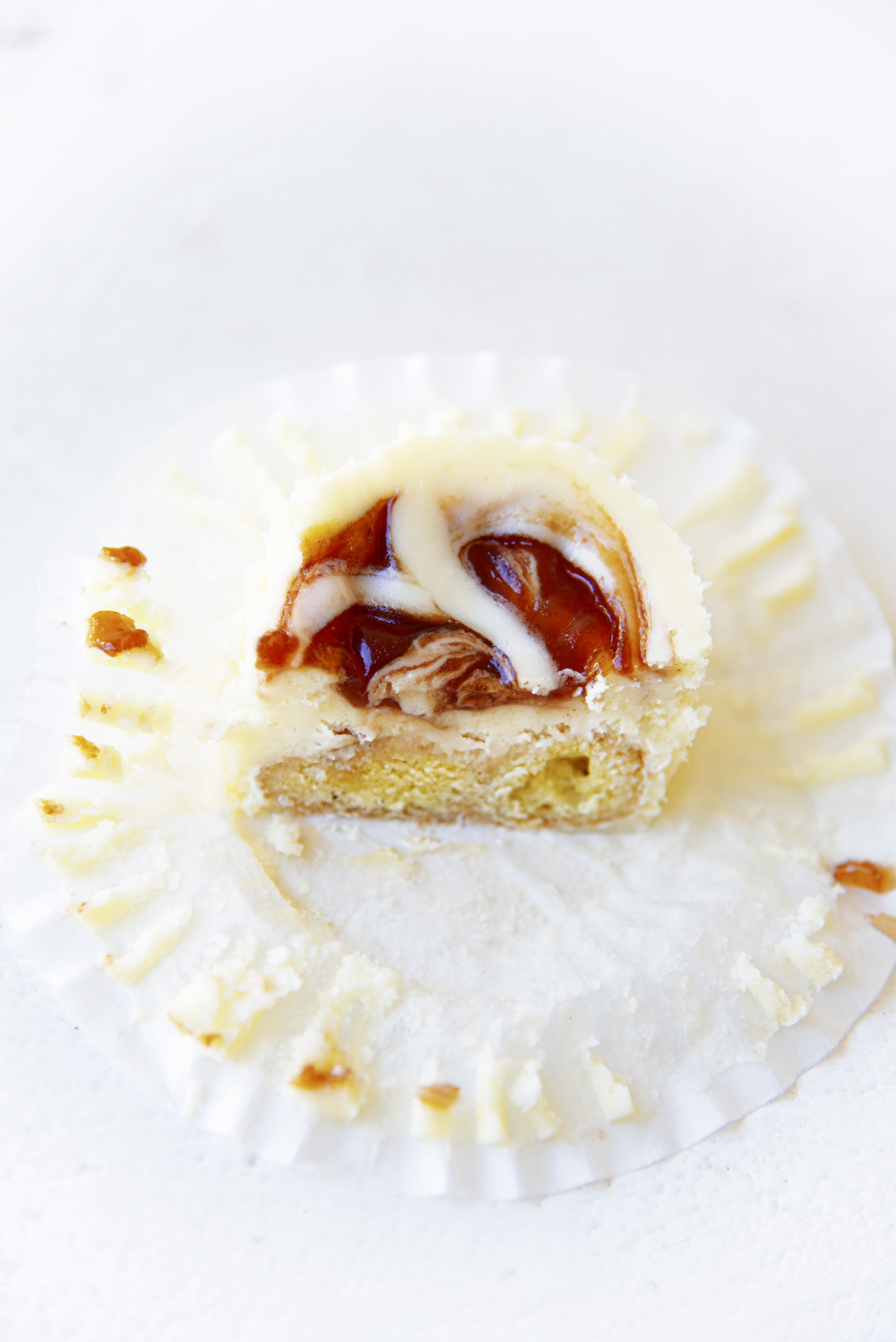 Overhead shot of half a cheesecake bite exposing the inside of it with the paper liner pulled out around it. 