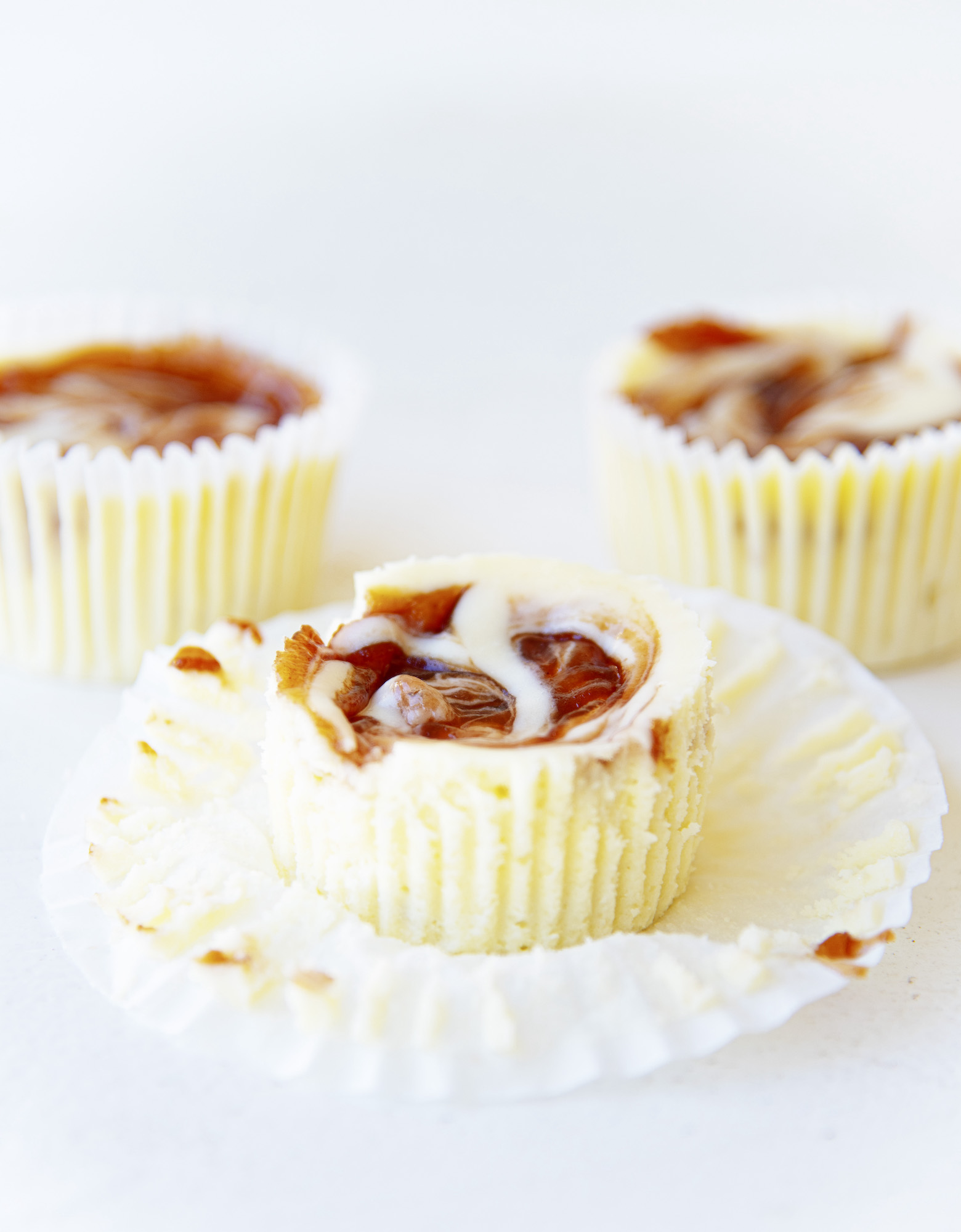 Three whole Powdered Jelly Donut Cheesecake Bites with focus on the center cheesecake bite. The paper liner is pulled down showing the sides of the bite.