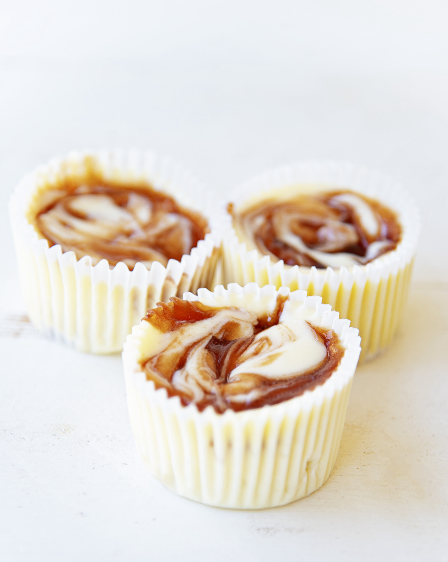 Three cheesecake bites with the focus on the swirled strawberry jelly tops. 