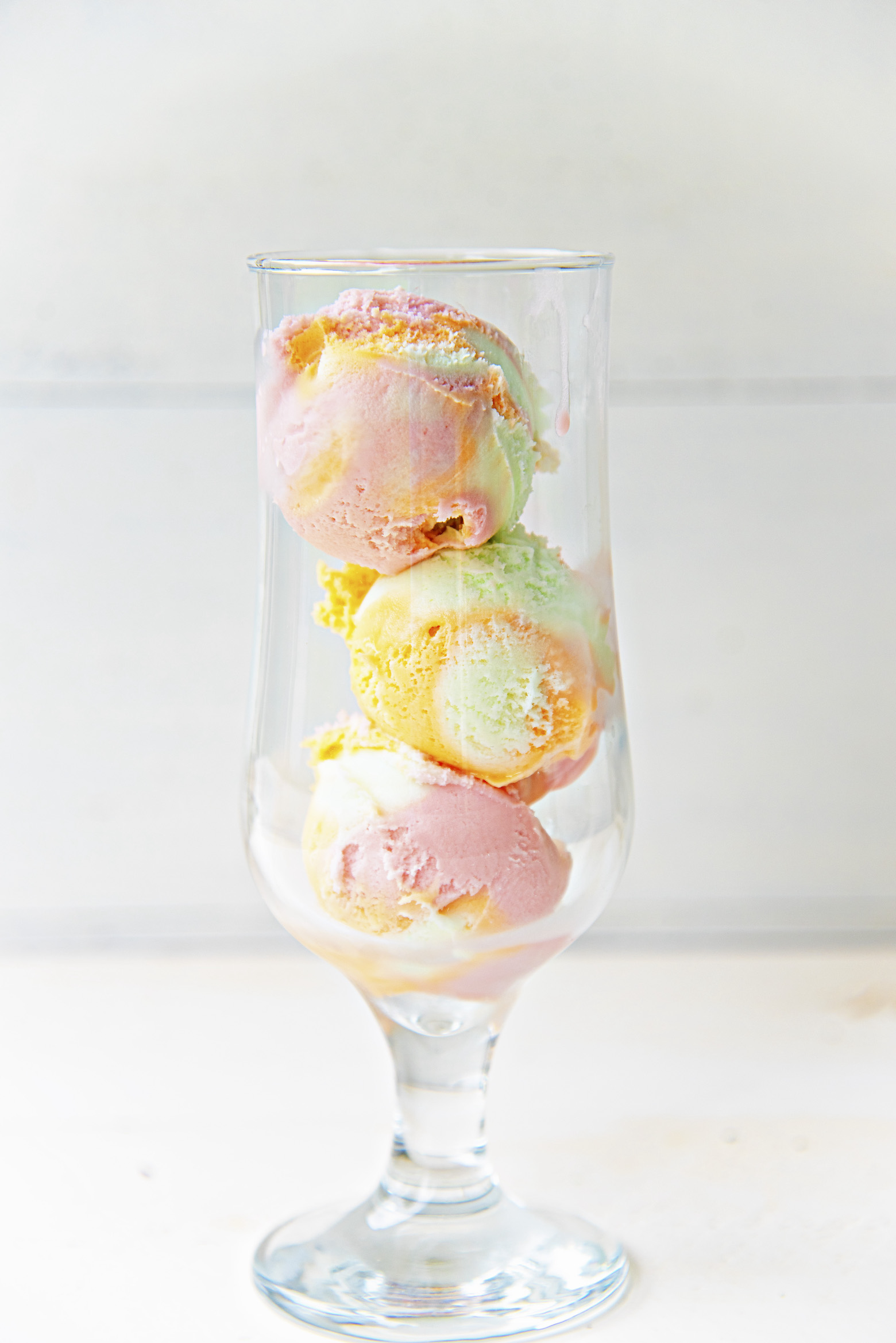 Glass with three scoops of rainbow sherbet stacked on top of each other. 