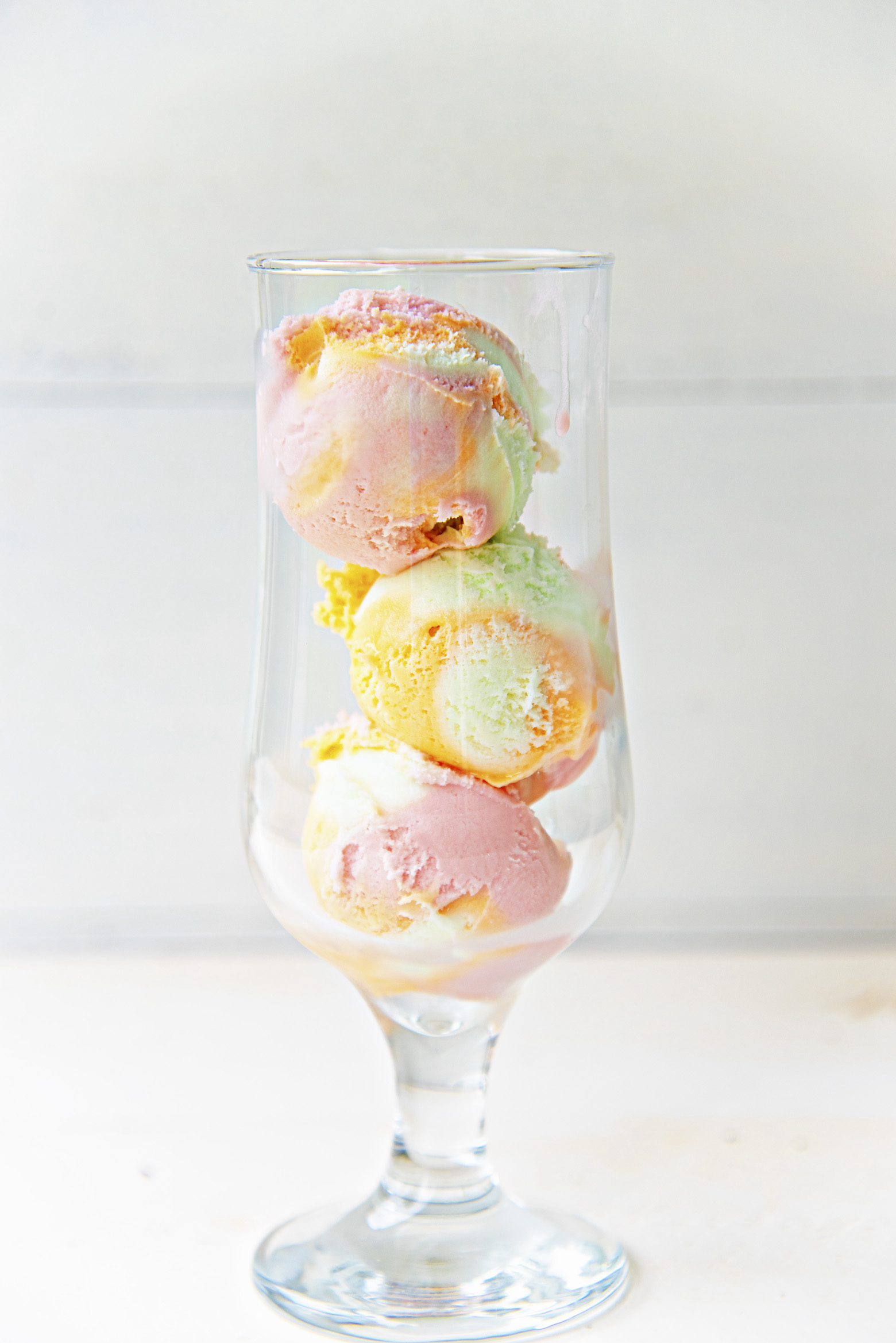 Glass with three scoops of rainbow sherbet stacked on top of each other.