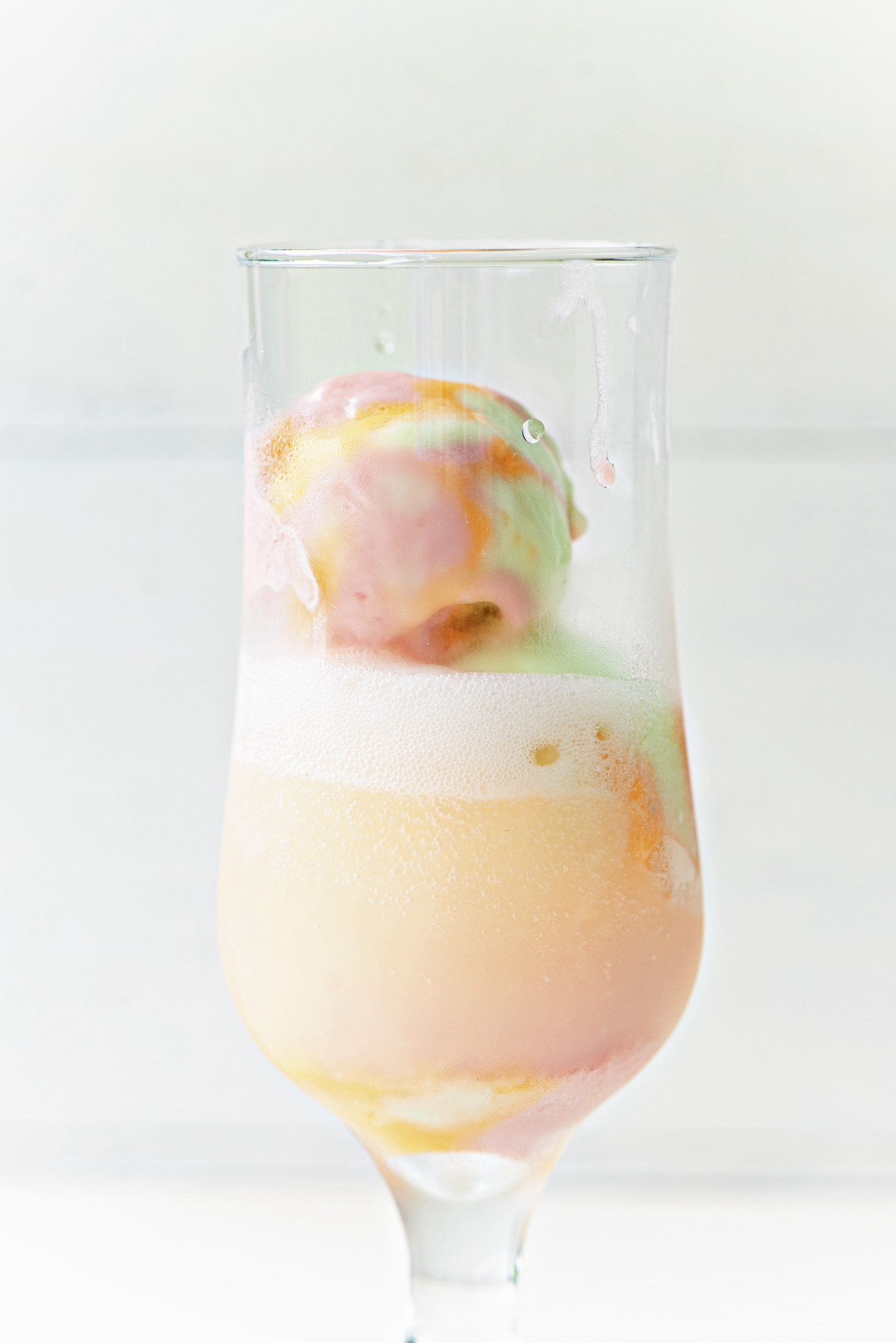 Glass with vodka and fizzy seltzer and scoops of rainbow sherbet with the focus on the top scoop of sherbet. 