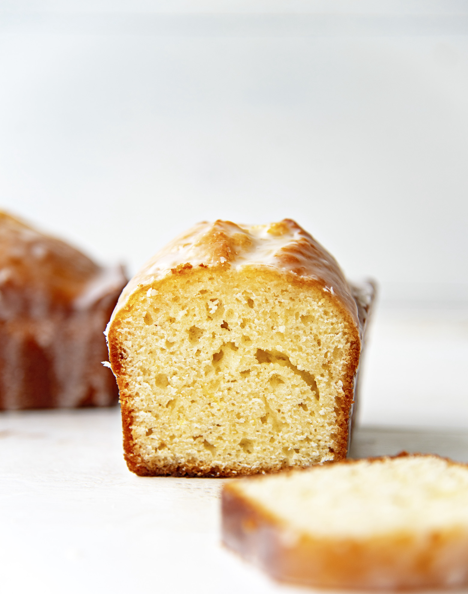 Loaf cut open to expose inside with a slice of the loaf cake in front of the cake. A whole loaf sits off to the left side of the cut loaf.