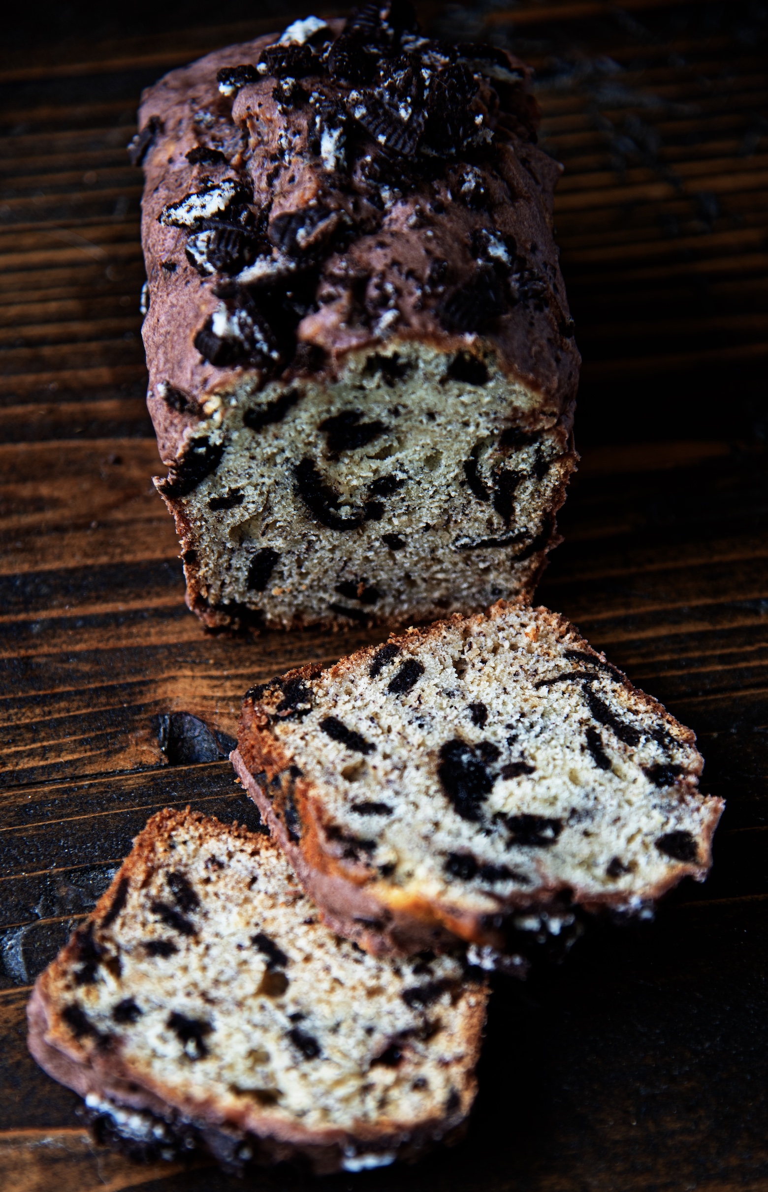 A mini loaf banana bread with pieces of Oreo cookie throughout it is sliced with two pieces out in front of it. 