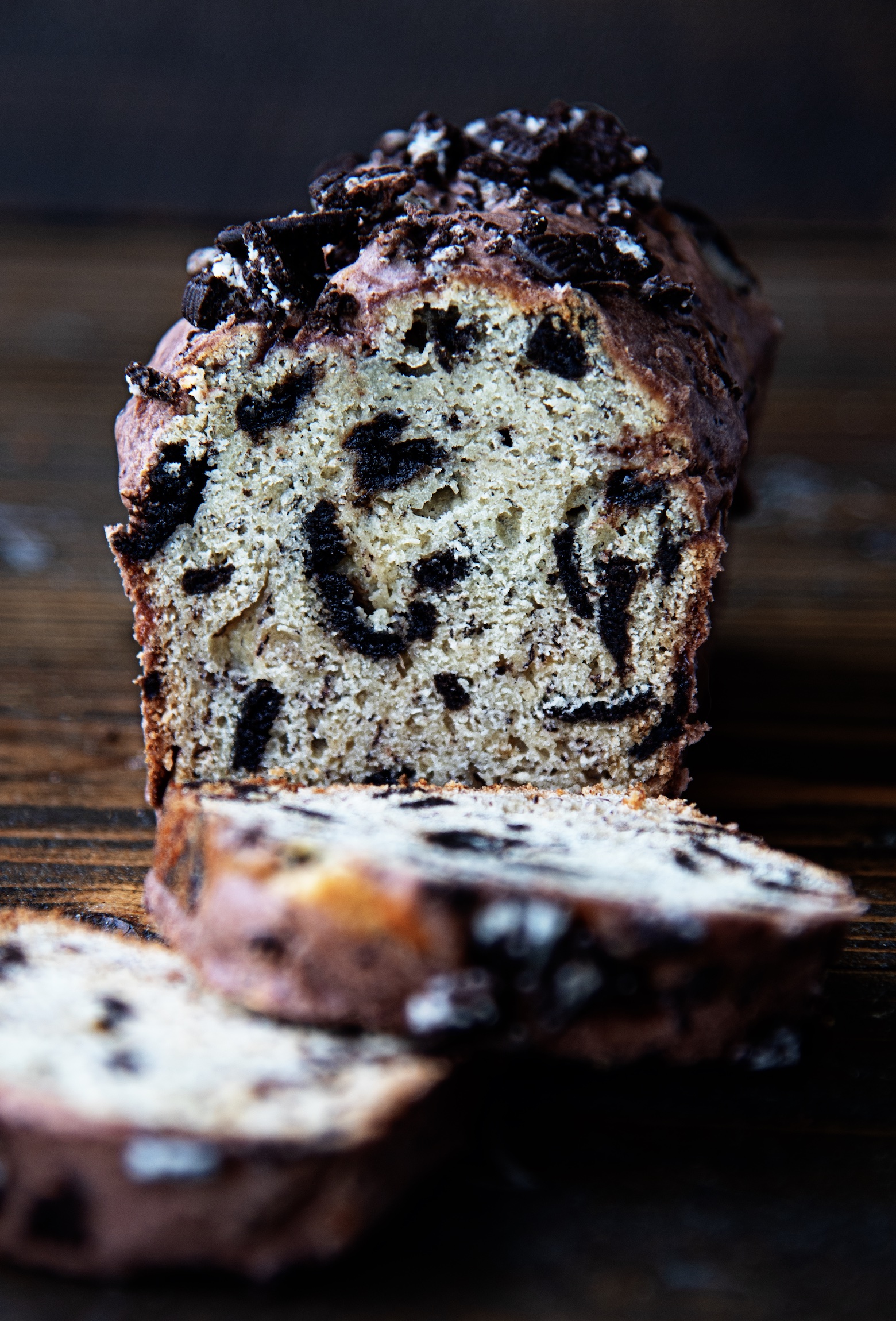 A mini loaf banana bread with pieces of Oreo cookie throughout it is sliced with two pieces out in front of it. Close up of the inside of the loaf. 
