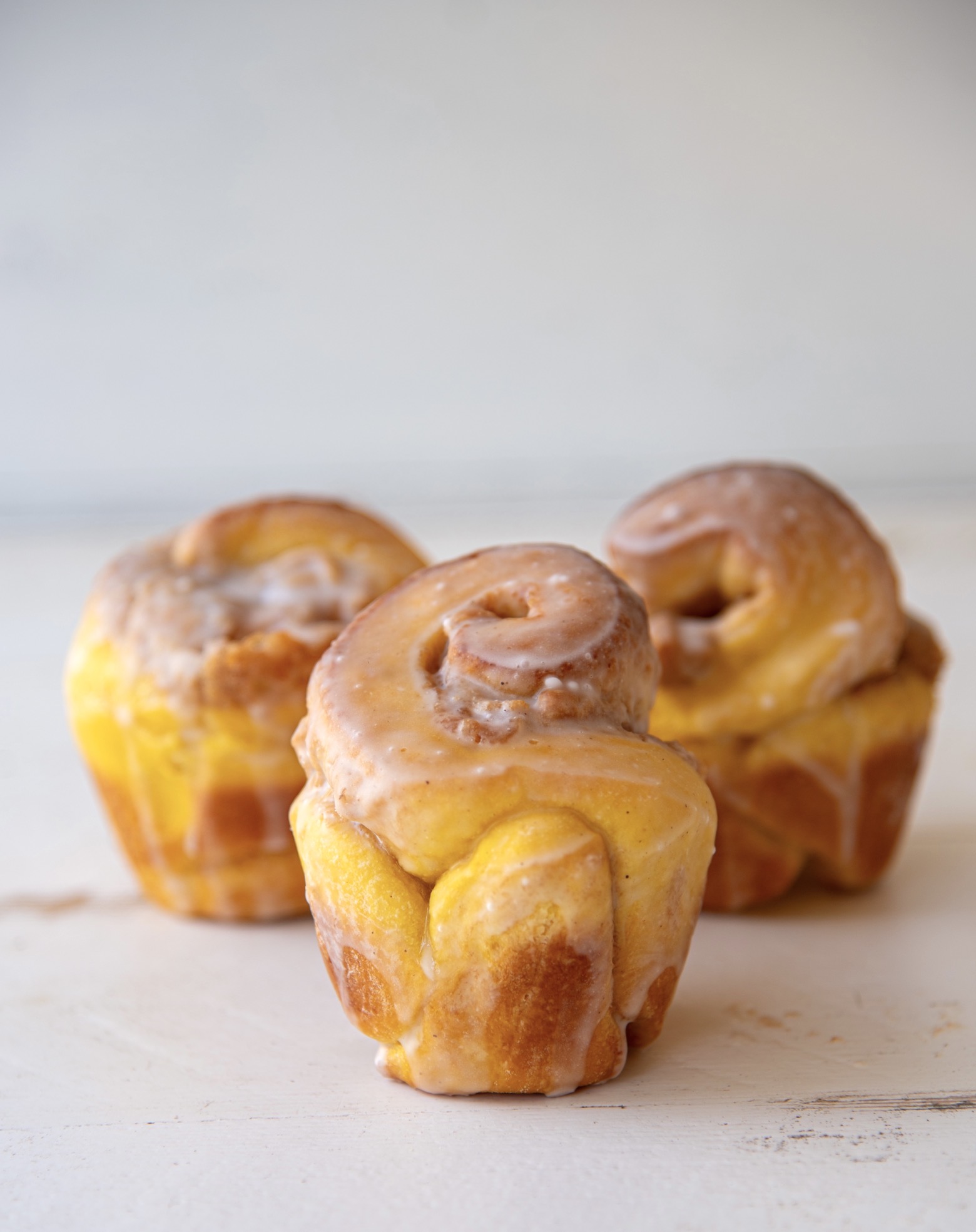 Three pumpkin brioche buns with the center bun being in focus and in front of the other two buns.