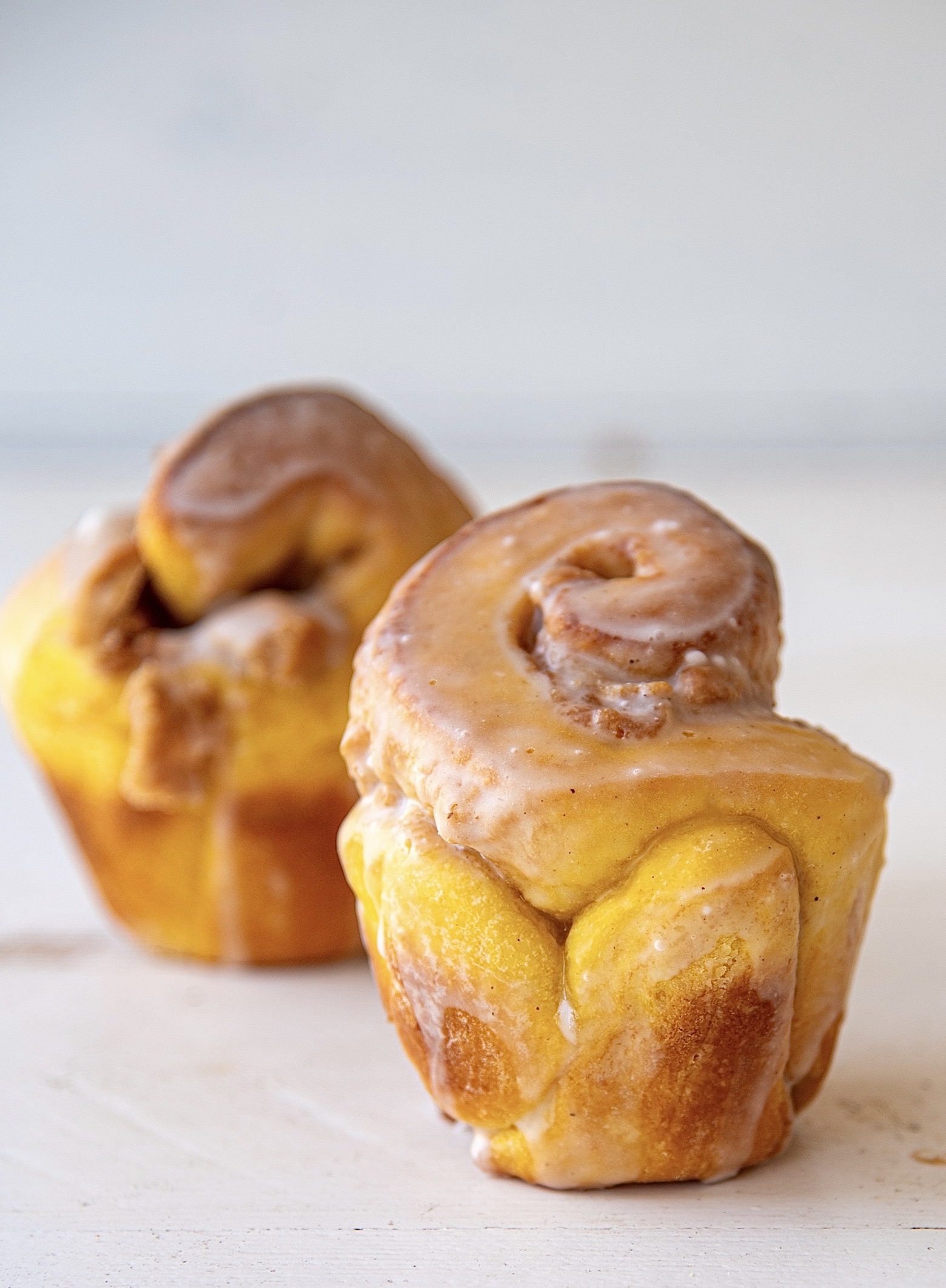 Two pumpkin brioche buns with one being up close and one behind. The bun that is in front is in focus. 