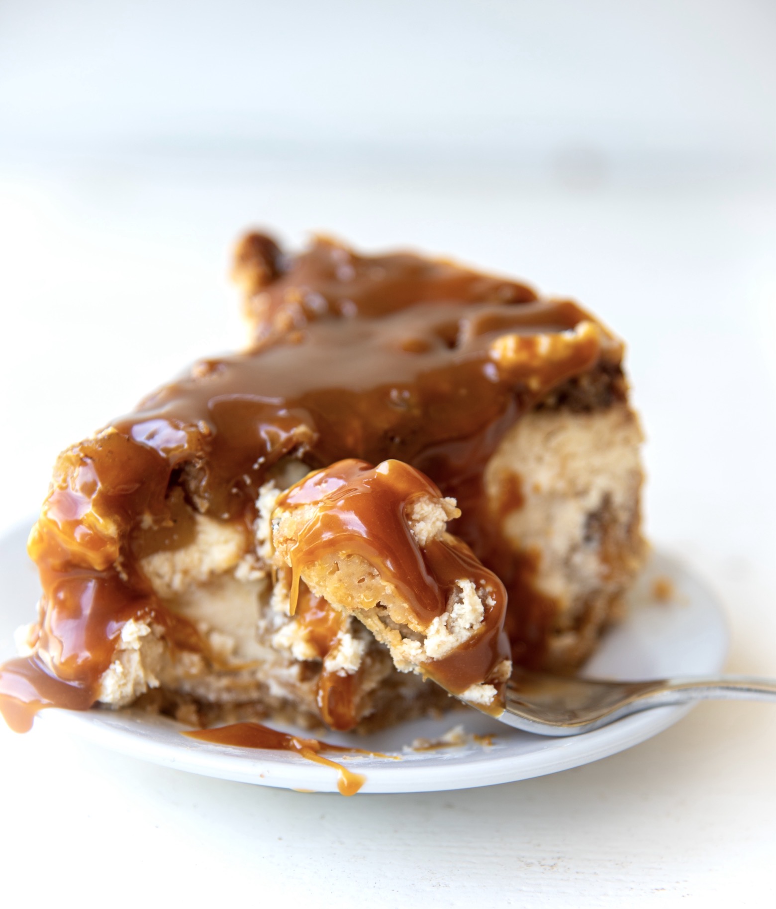 Side view of a slice of Apple Crumb Pie Cheesecake on a small white plate with caramel drizzle.