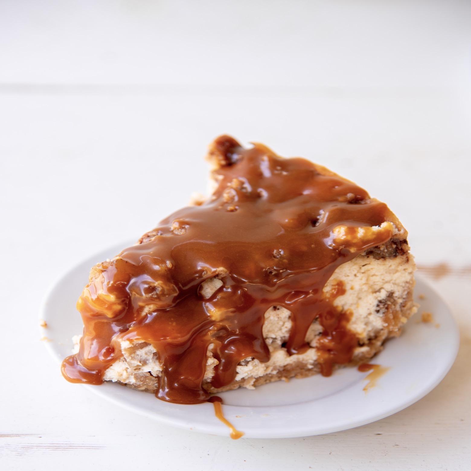 Side view of a slice of Apple Crumb Pie Cheesecake on a small white plate with caramel drizzle.