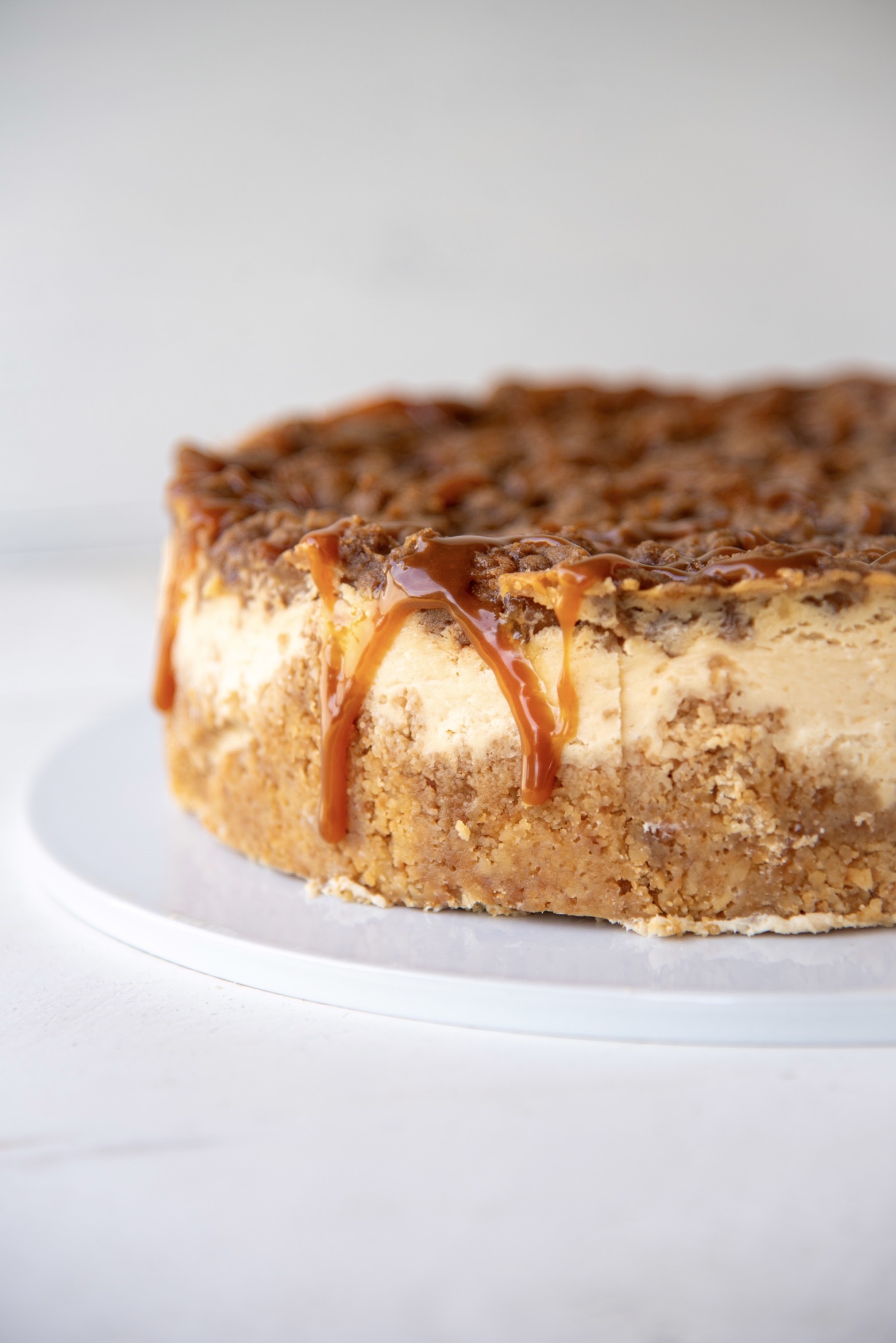 Side view of Apple Crumb Pie Cheesecake on a cake plate with caramel drizzling down the side. 