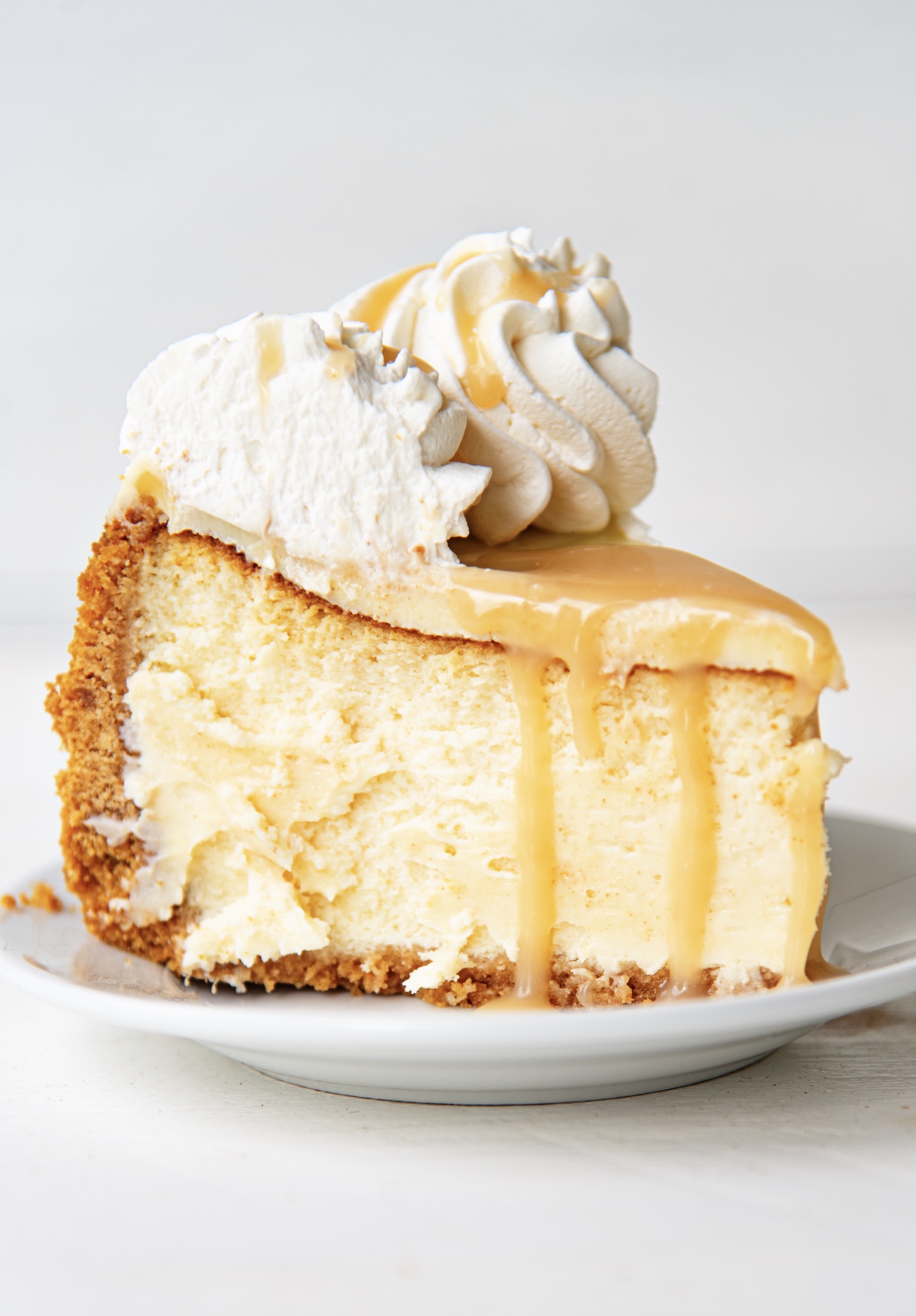 Single slice of cheesecake with caramel sauce dripping down topped with whipped cream. 