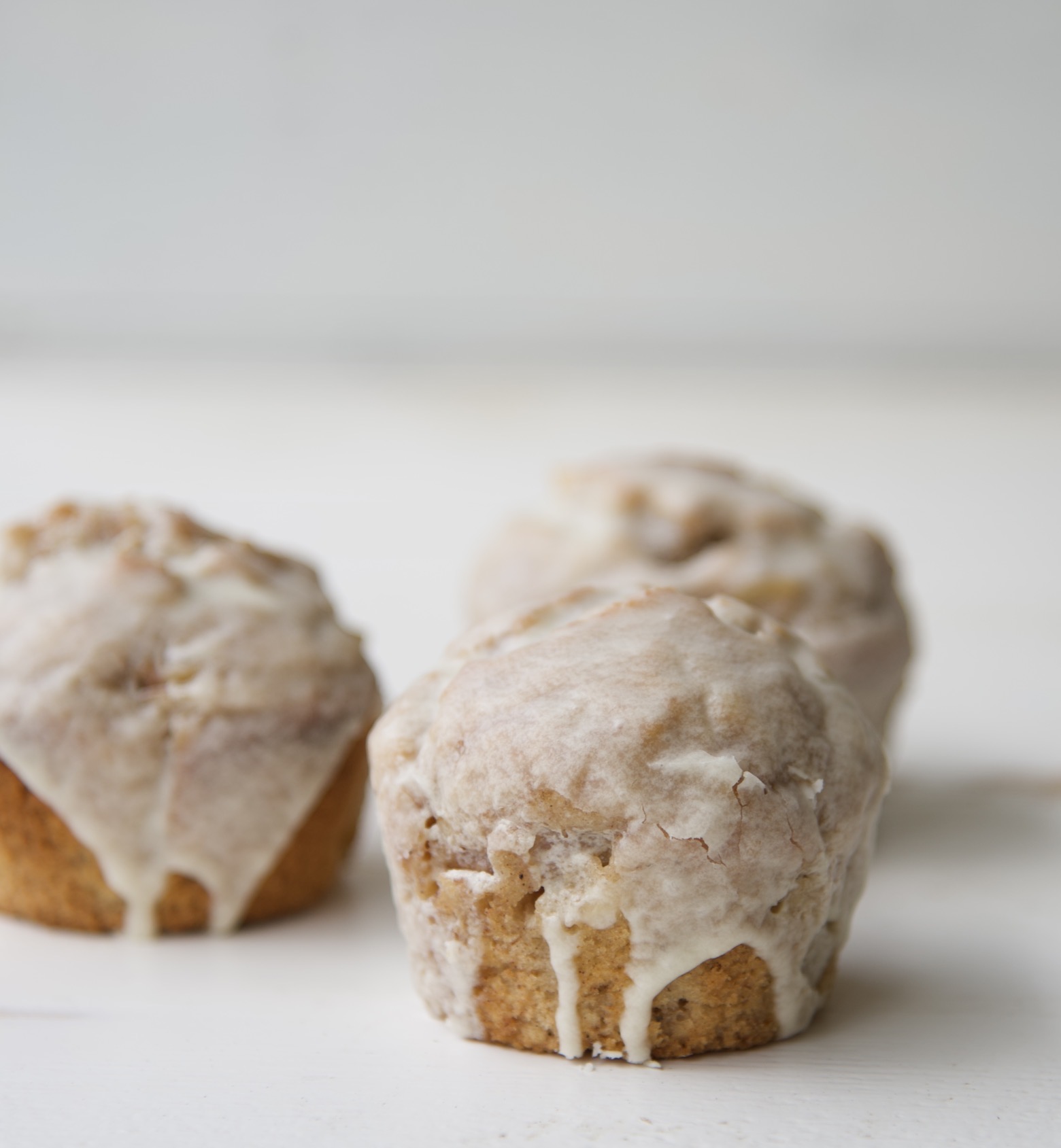 Three apple pie Ala mode muffins with glaze dripping down.