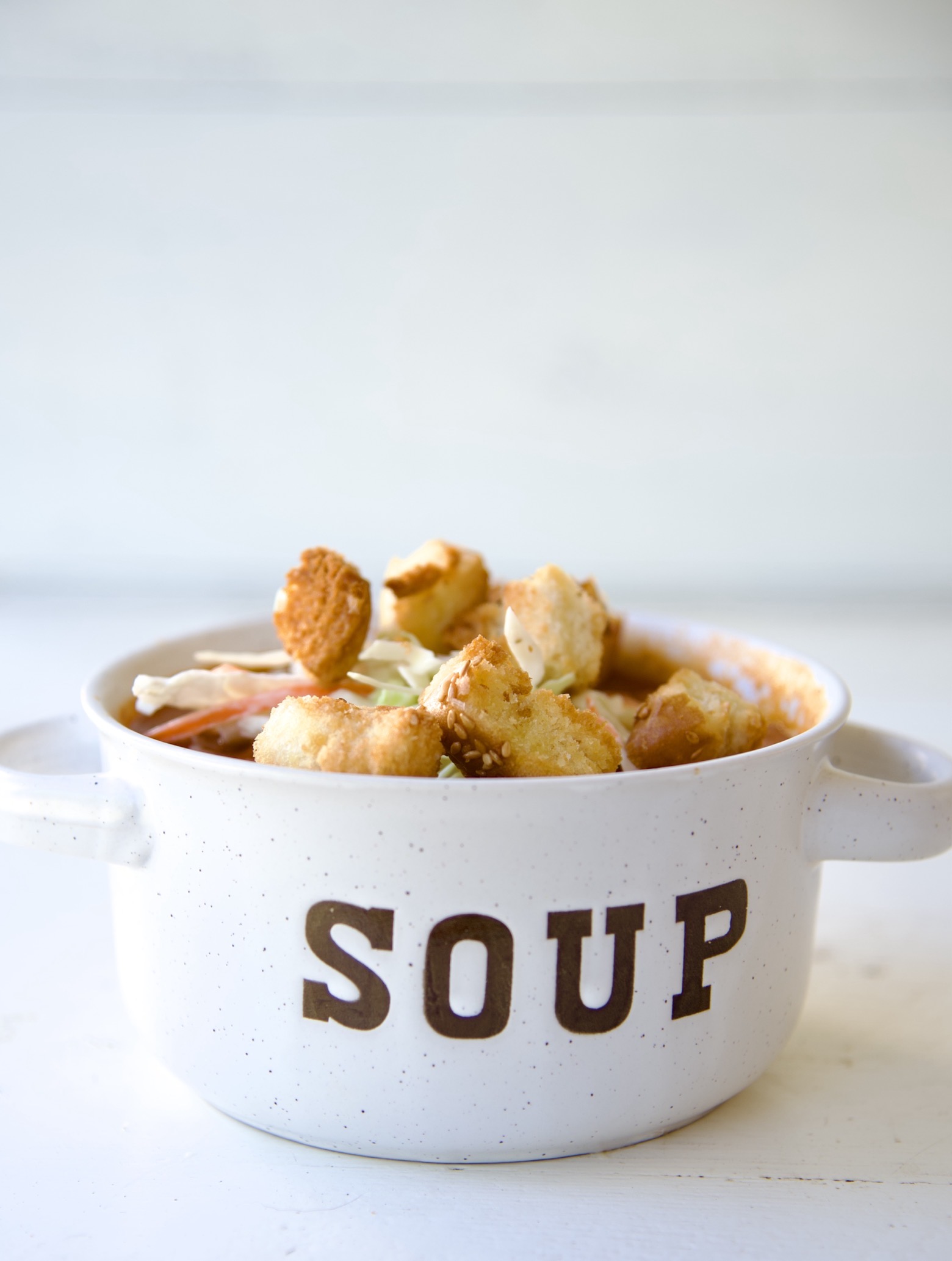 Side view of the soup in a bowl that reads soup and has coleslaw and croutons piled on top. 